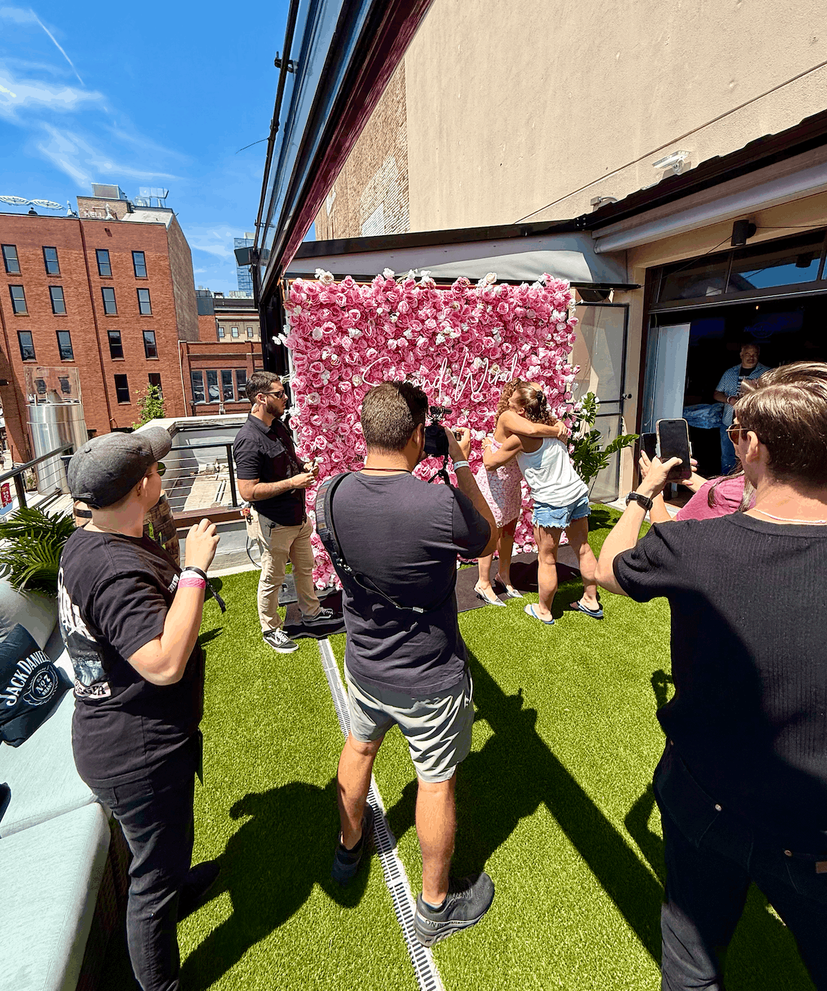 Media photographers capturing a country music artist meet-and-greet event in front of a pink flower wall backdrop with a custom neon sign on the rooftop patio at Hard Rock Cafe Nashville during CMA Fest.