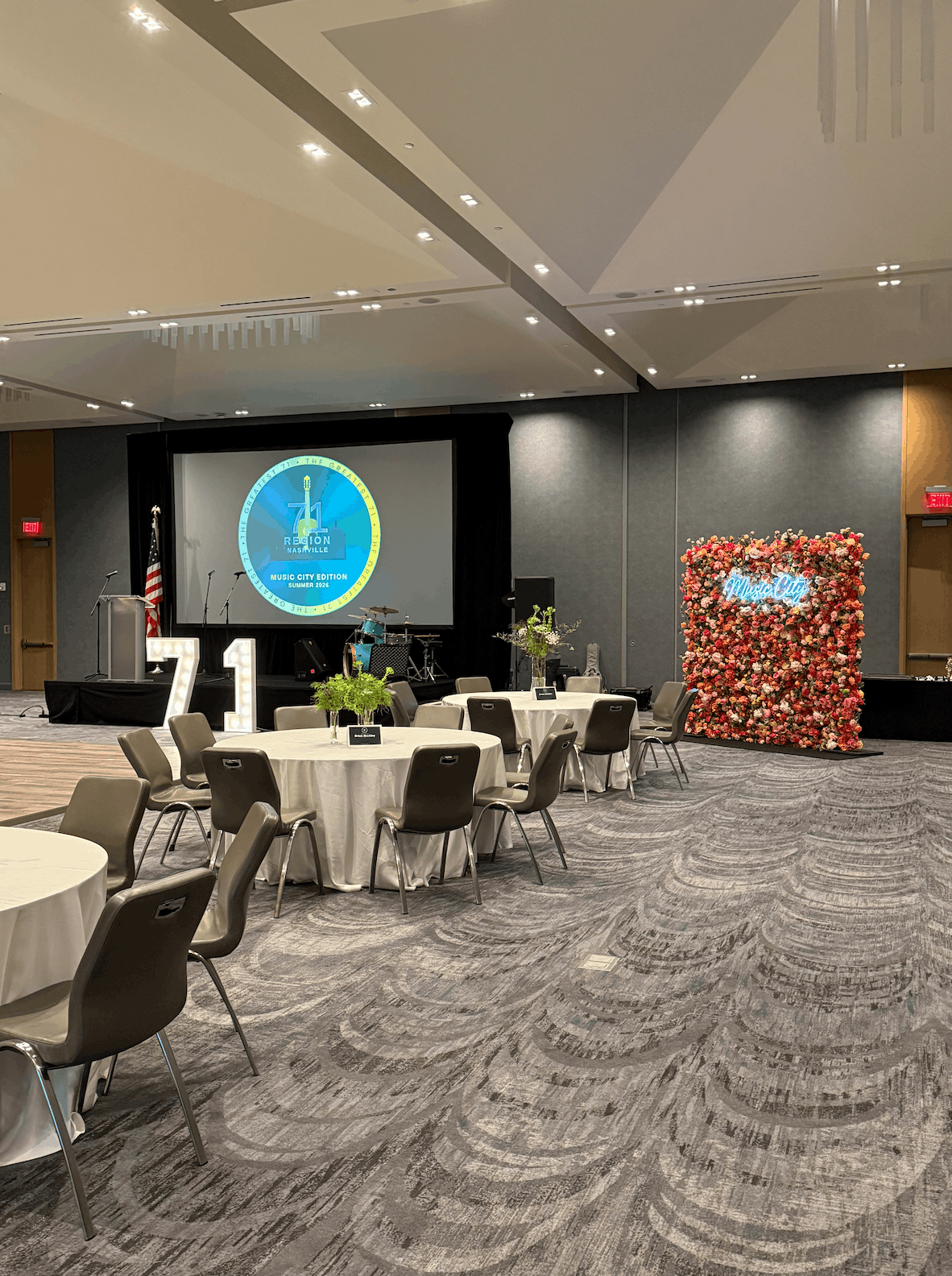 A vibrant, multi-colored wildflower backdrop wall featuring a bright blue neon sign reading Music City, set up for a corporate event at The Joseph Hotel in Nashville.