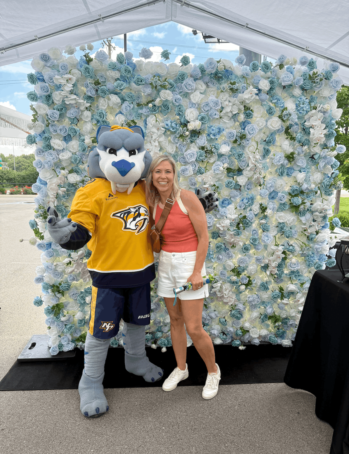 Penelope blue and white 3D silk flower wall backdrop setup with Gnash the Nashville Predators mascot at an outdoor corporate event
