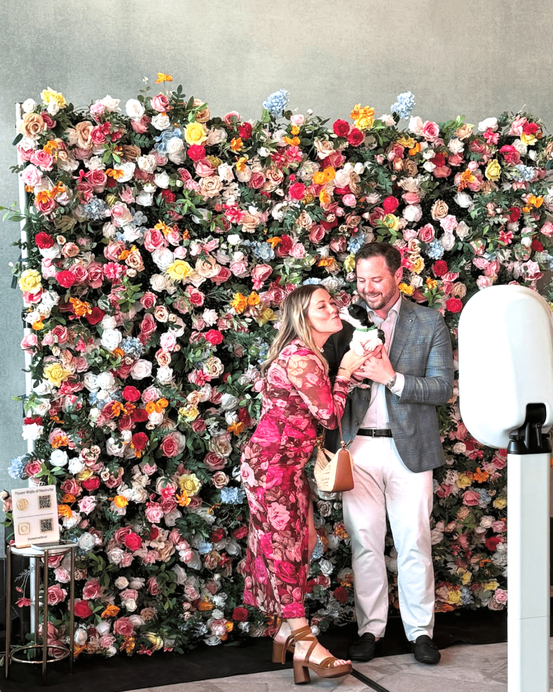 Luxury colorful flower wall rental in Nashville featuring premium silk florals, used as a corporate event photo booth backdrop for a couple and their dog.