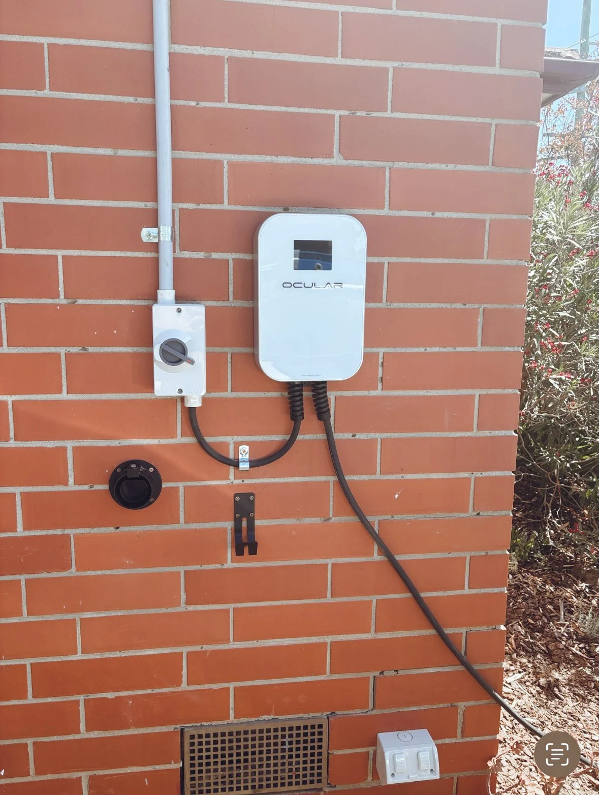 Electric vehicle charging station on brick wall with plug and meter.