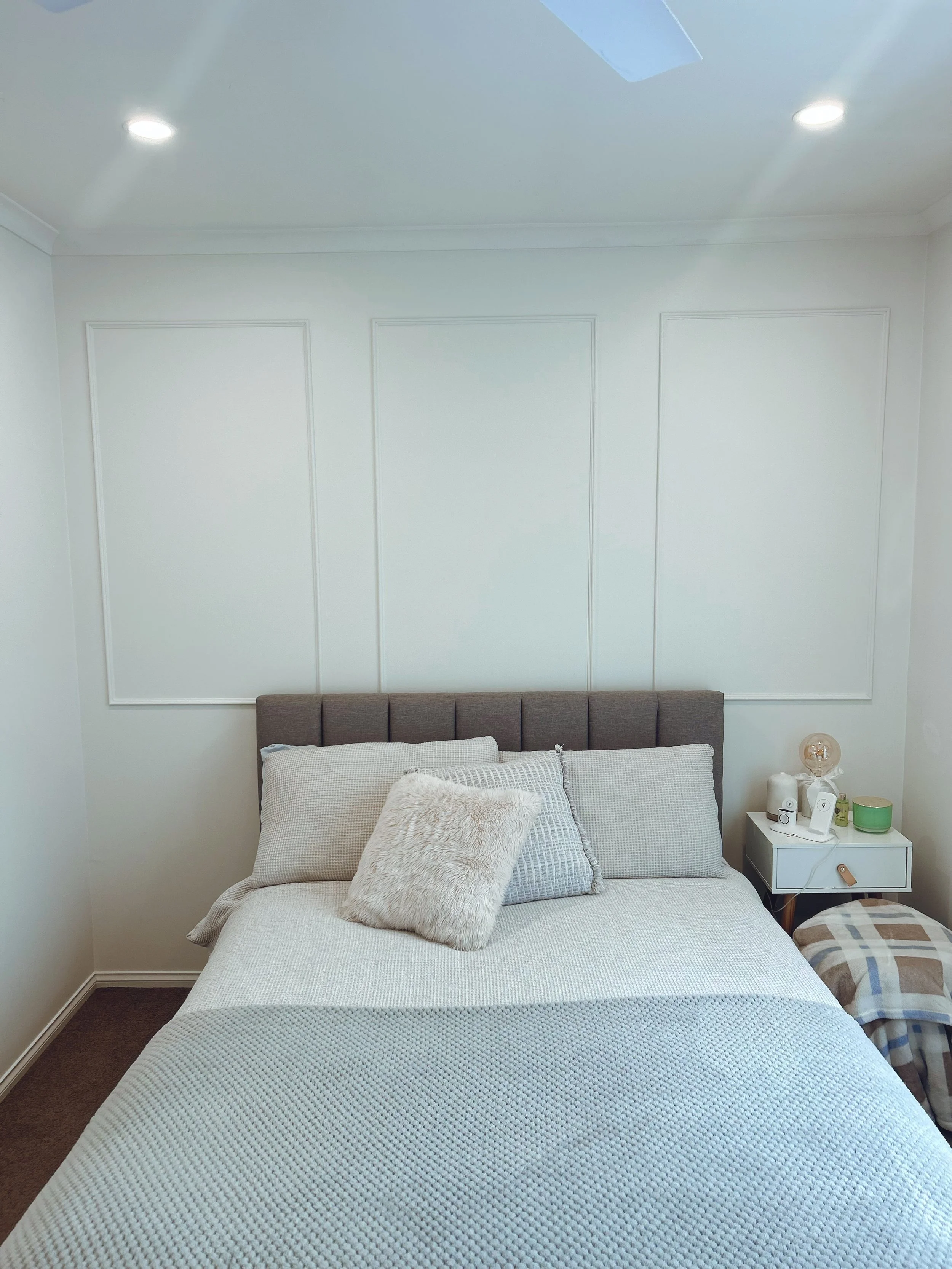 A cozy bedroom with a neatly made bed, a headboard, pillows, and a bedside table with a lamp, clock, and other items.