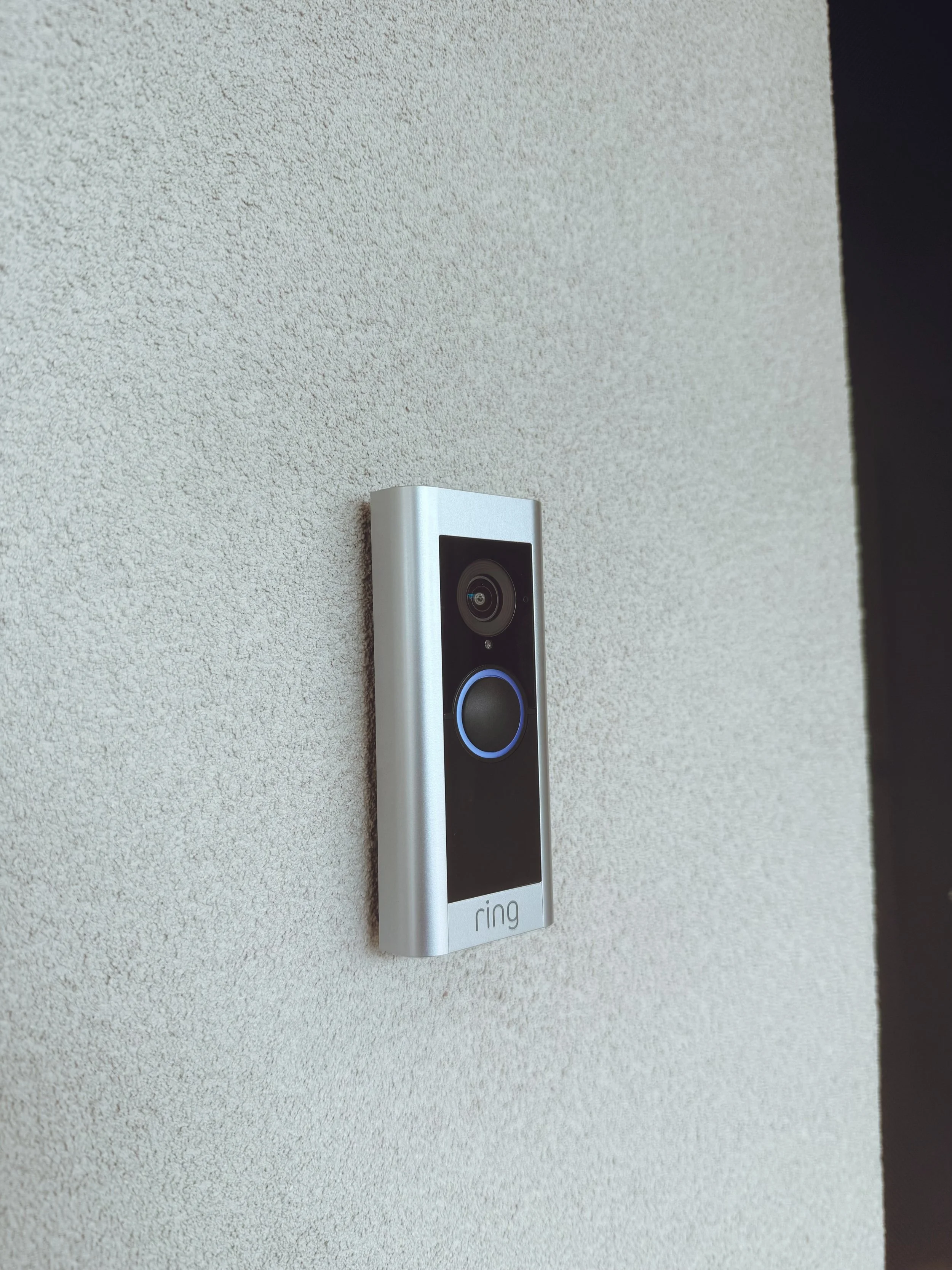 A Ring video doorbell mounted on a textured beige wall.