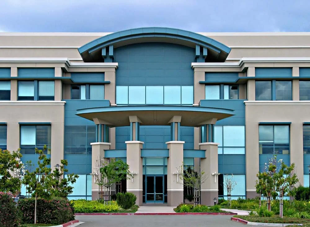 Corporate headquarters front entrance with mature trees and lush shrubs, showcasing professional commercial landscape design that enhances brand image and curb appeal.