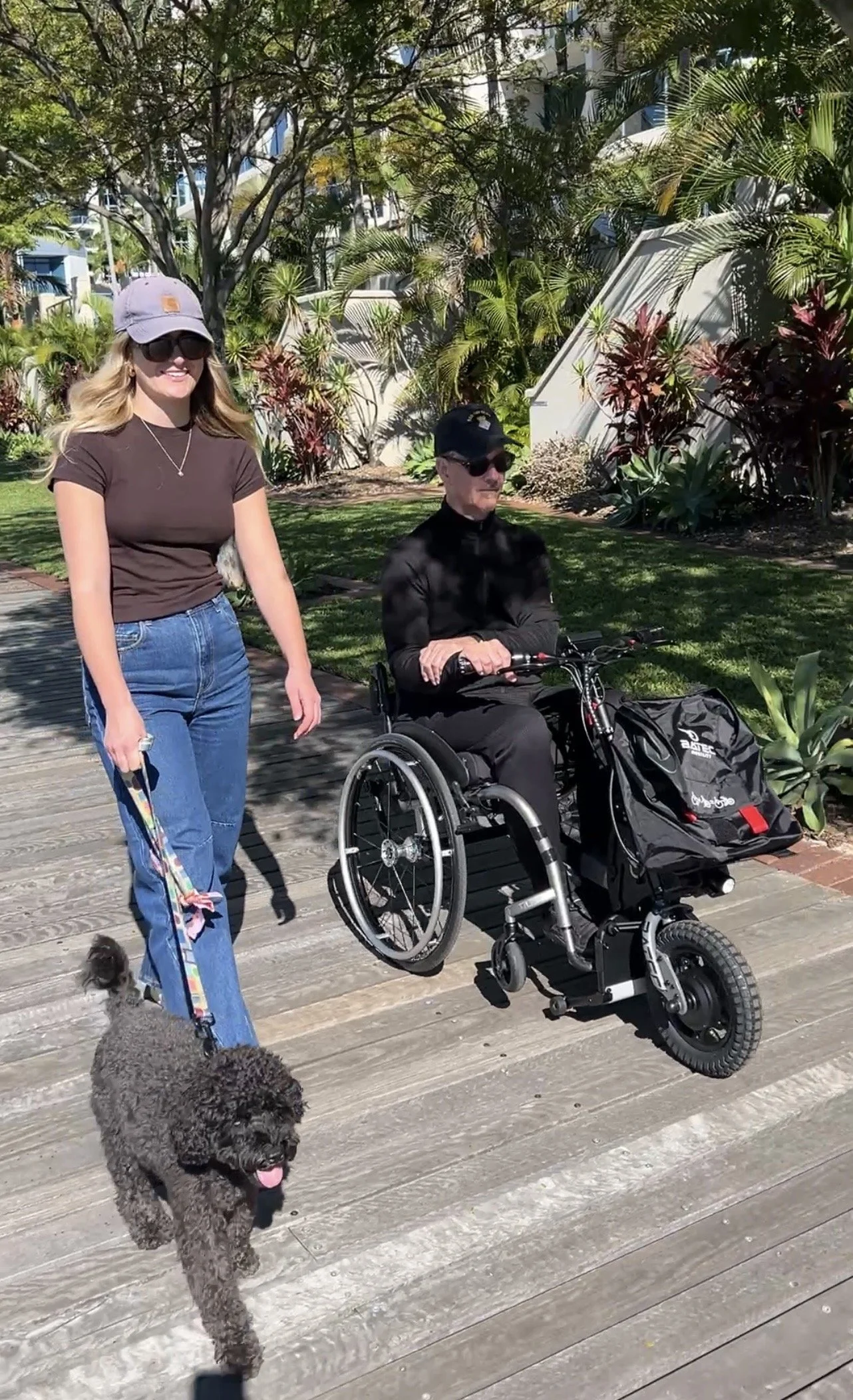 Man using a wheelchair after a spinal cord injury enjoying an outdoor walk with his daughter and dog, demonstrating independence and community participation.