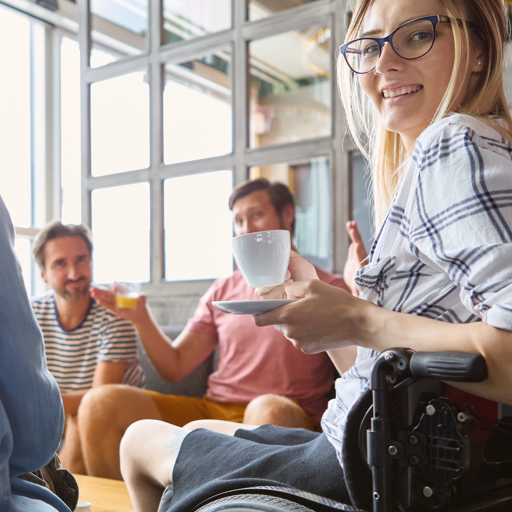 Woman using a wheelchair enjoying coffee and social connection with friends, representing returning to meaningful activities and community participation