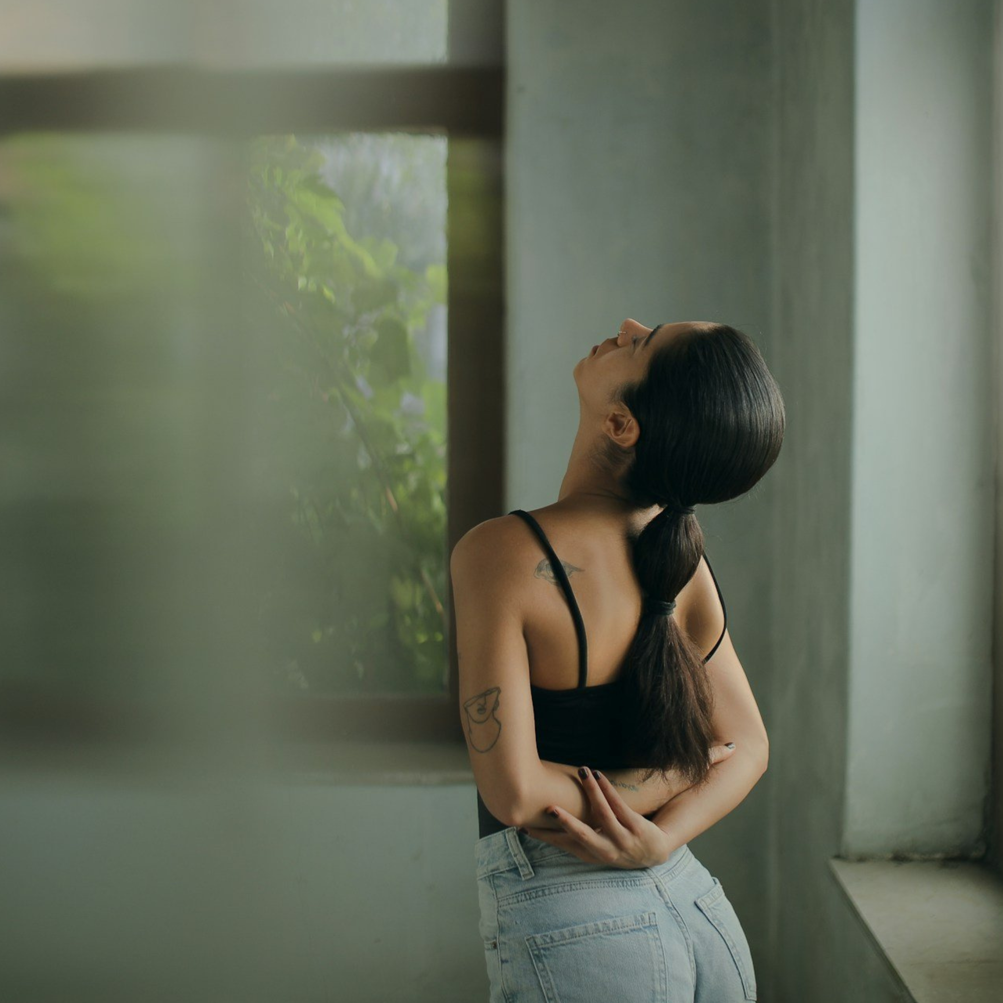 Person standing near a window performing a gentle stretch to support movement and recovery while managing persistent pain
