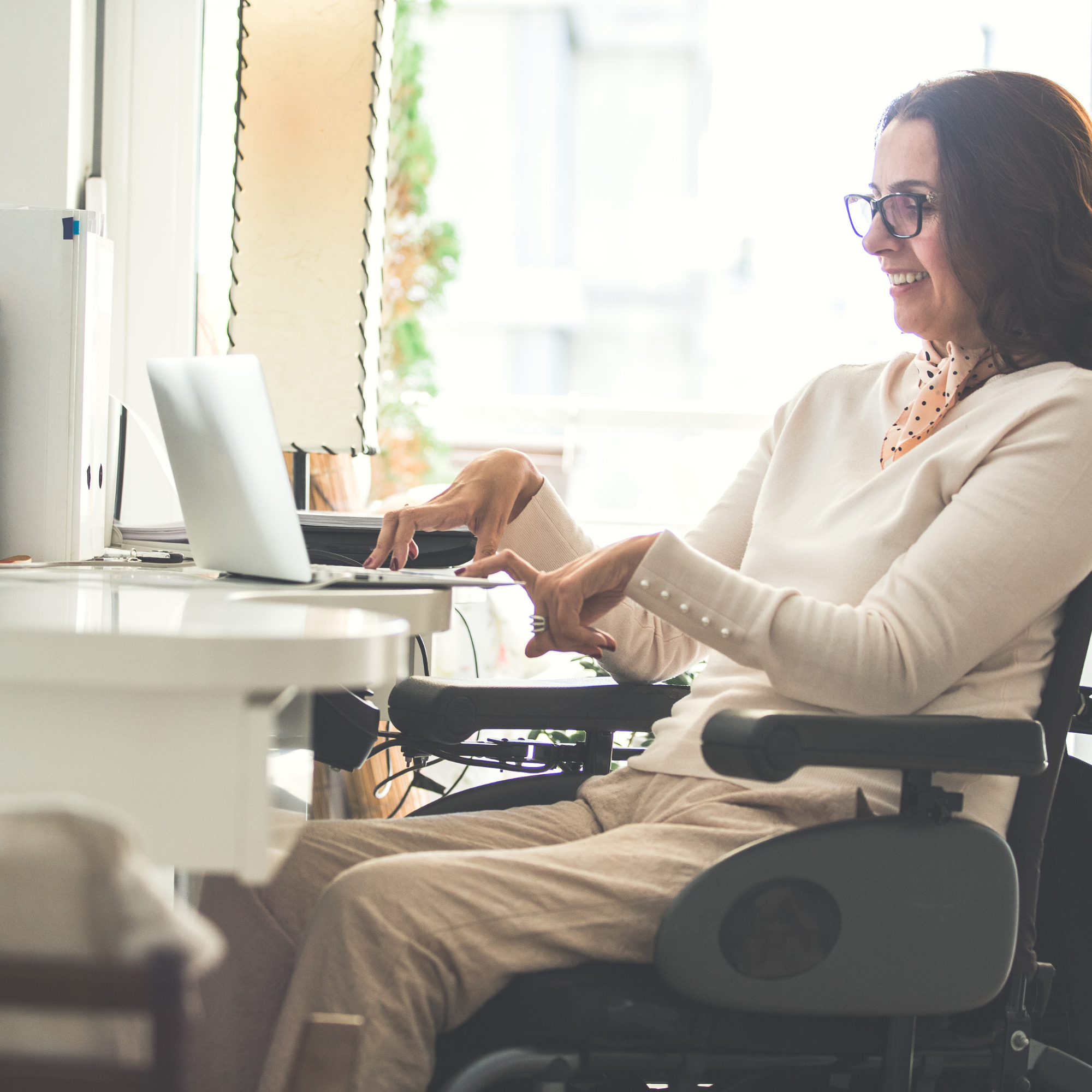 Woman using a wheelchair confidently working on a laptop in an accessible home office environment