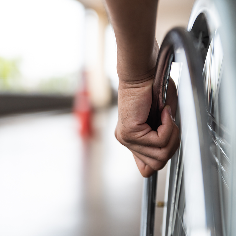 Close-up of a person’s hand pushing a wheelchair wheel, representing spinal cord injury rehabilitation and mobility support