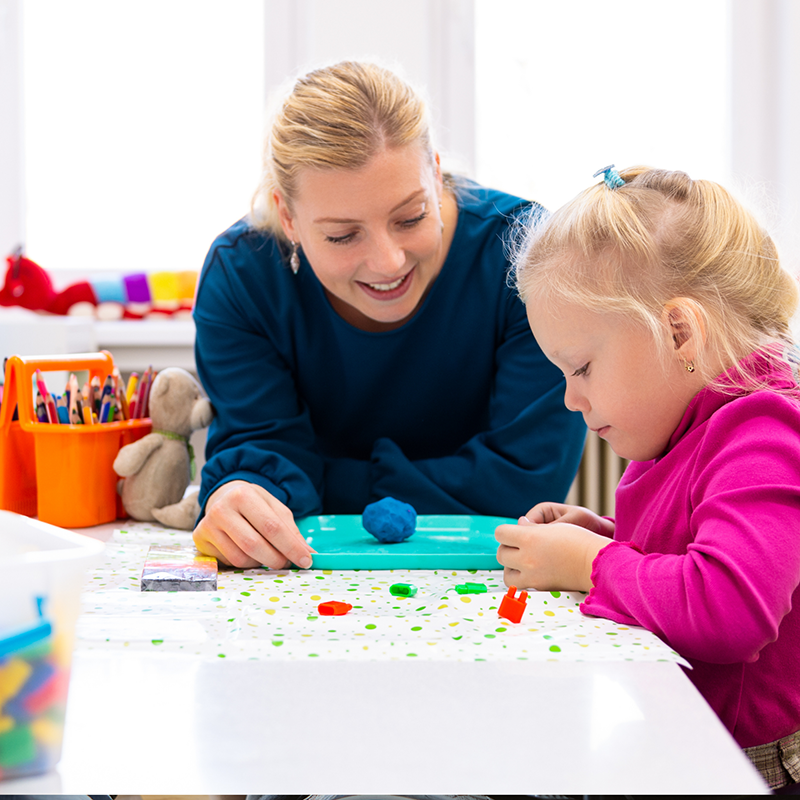 Paediatric occupational therapist supporting a young child during a play-based therapy activity at a table
