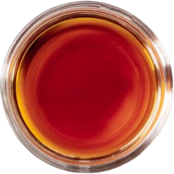Close-up view of a small glass used for drinking, filled with dark amber liquid, possibly whiskey or tea.