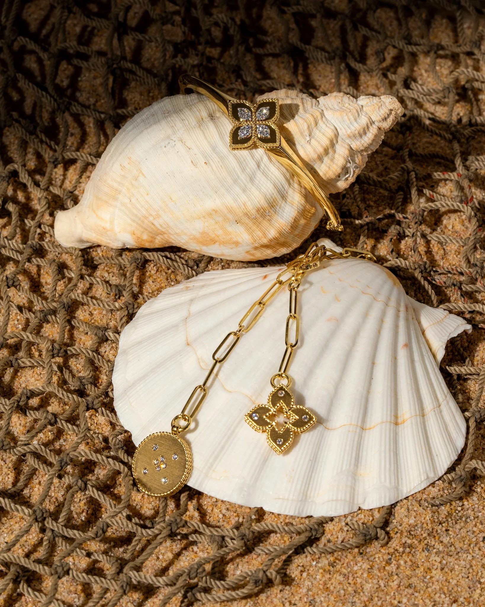 Gold jewelry with butterfly and floral designs, placed on seashells against a textured surface.