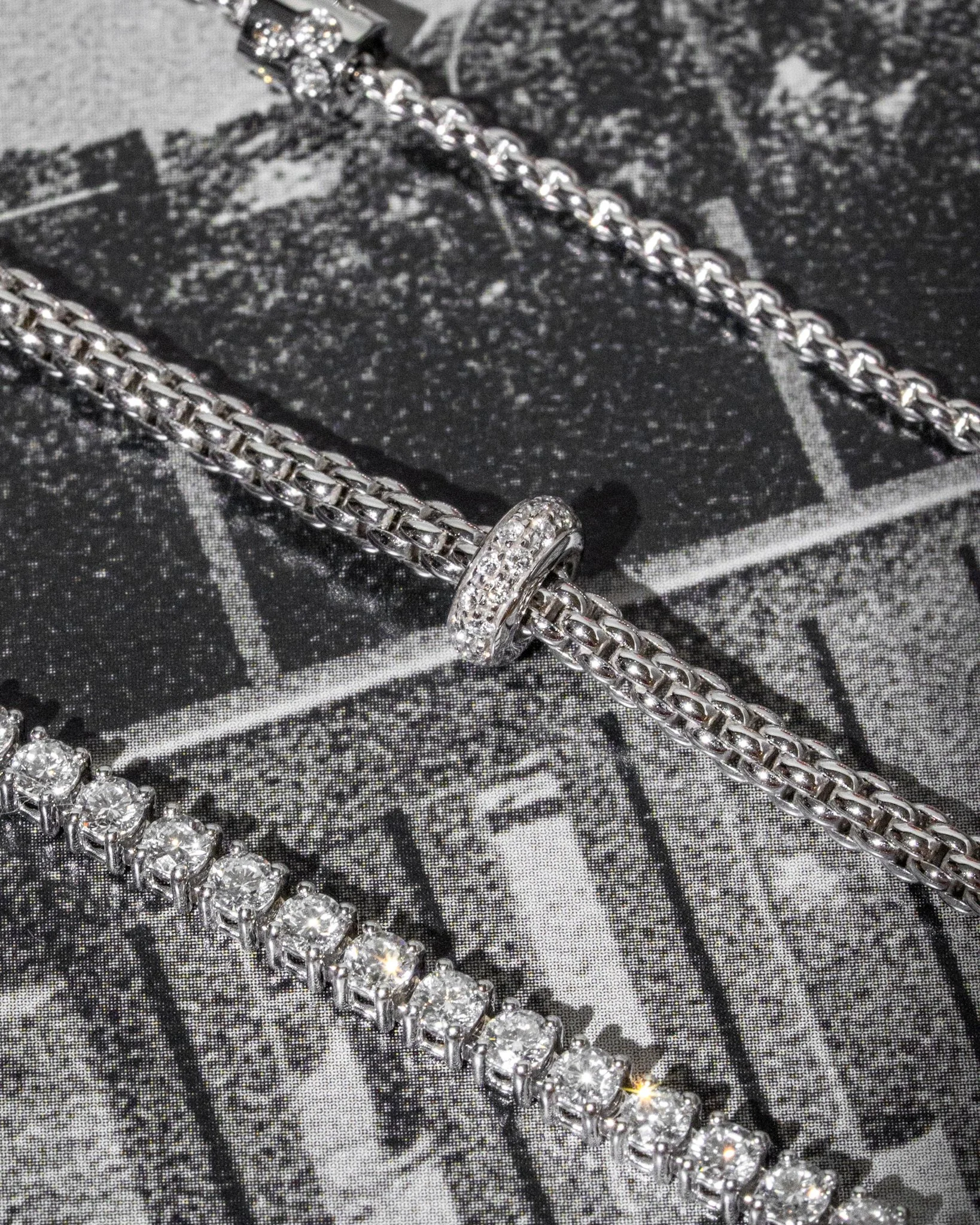 Close-up of a silver chain necklace with a large rhinestone clasp, on a black and white textured surface.