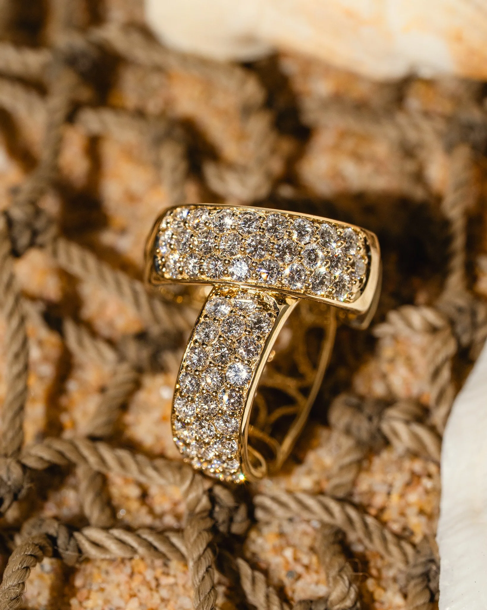 Close-up of a gold ring encrusted with numerous small sparkling diamonds, resting on a textured woven surface.