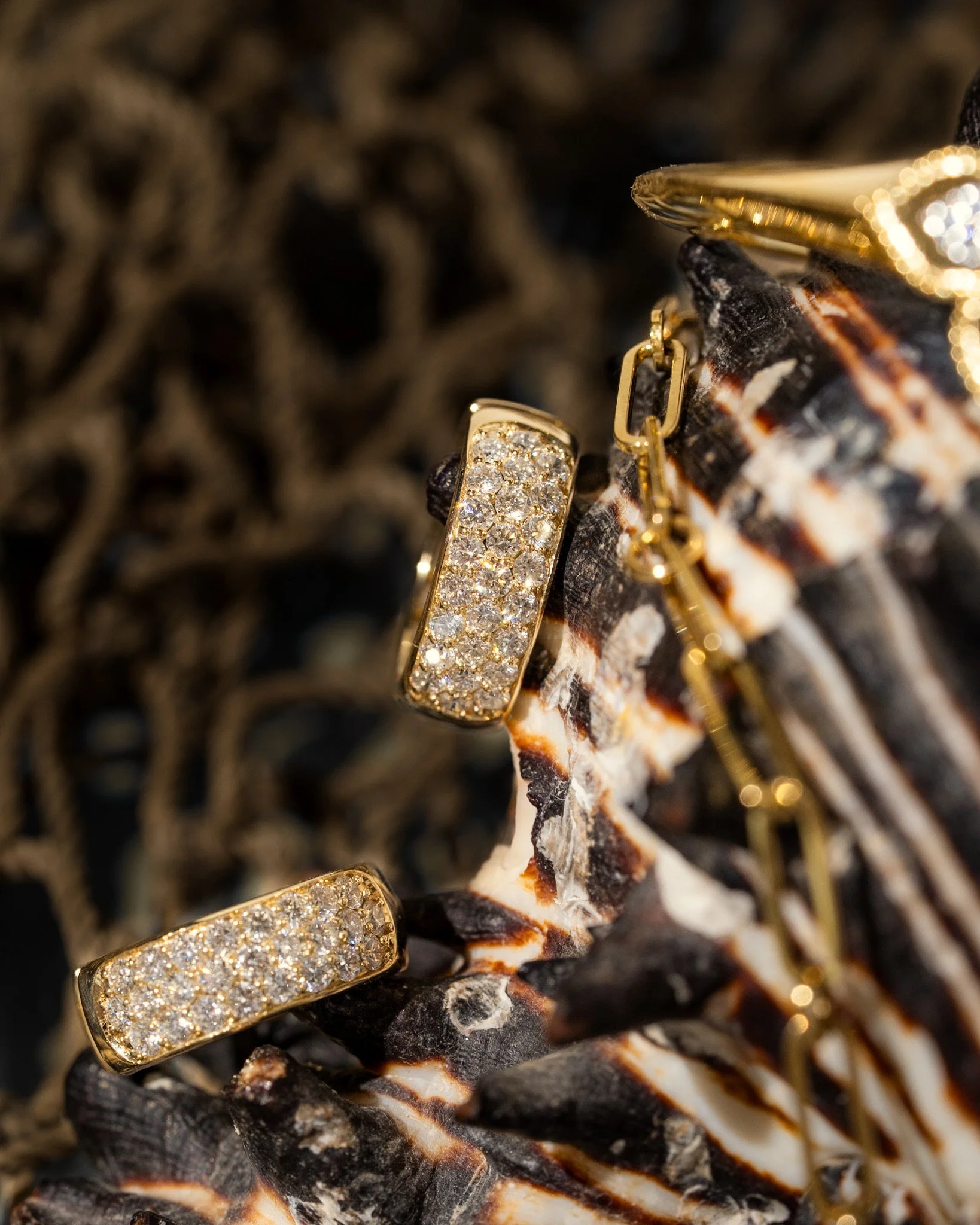 Gold earring with embedded diamonds resting on a rock with black and white patterns.