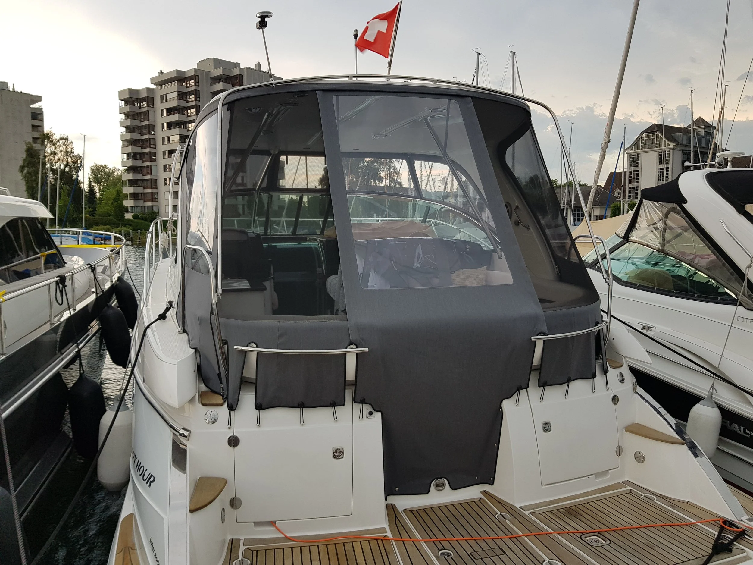 Ein Motorboot im Hafen mit Liegeplätzen auf beiden Seiten. Ein Gebäude und eine rote Flagge im Hintergrund.