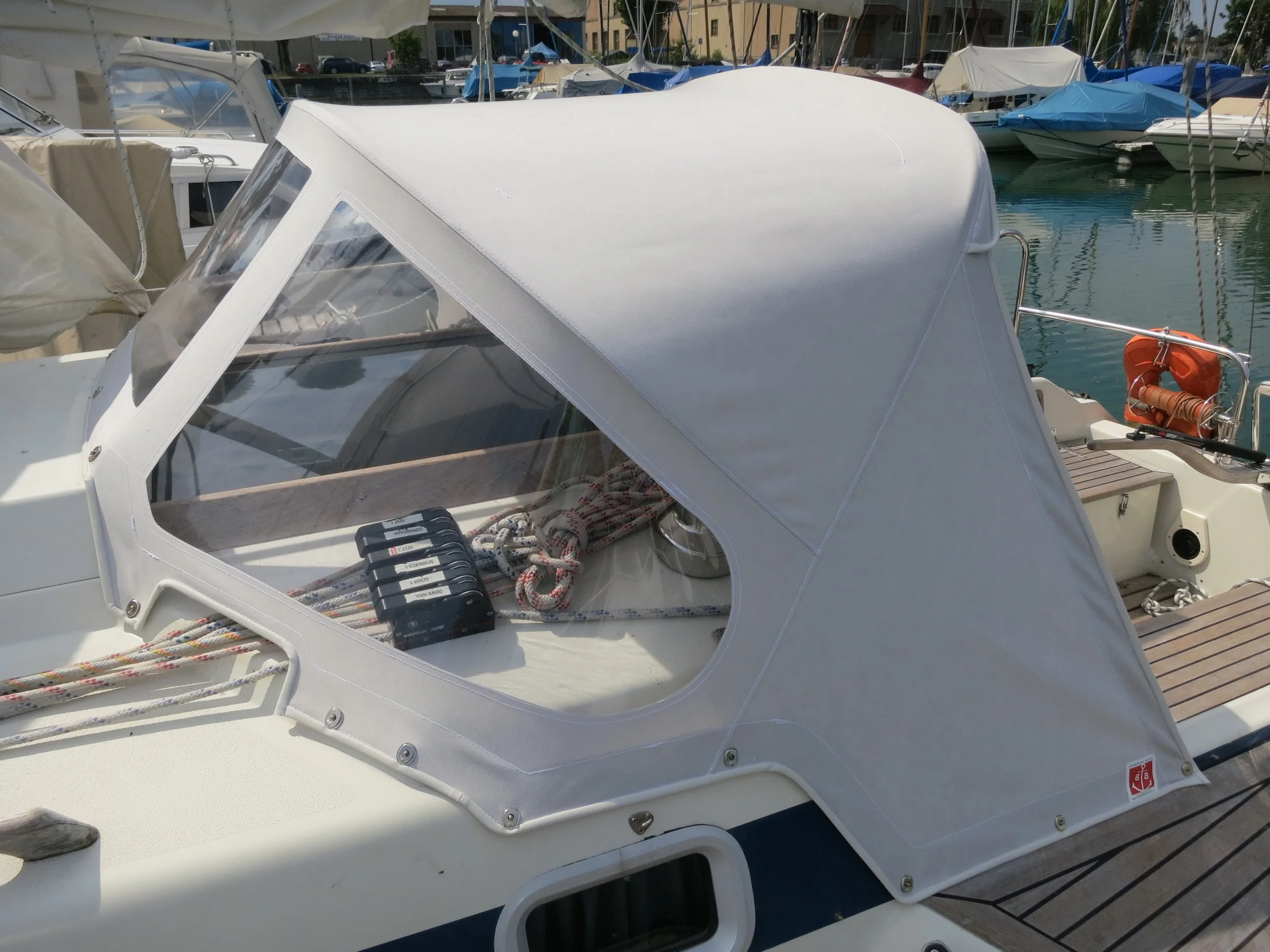 Weisse Sprayhood auf einer Yacht im Hafen mit Seilen und einer Rettungsboje im Hintergrund.