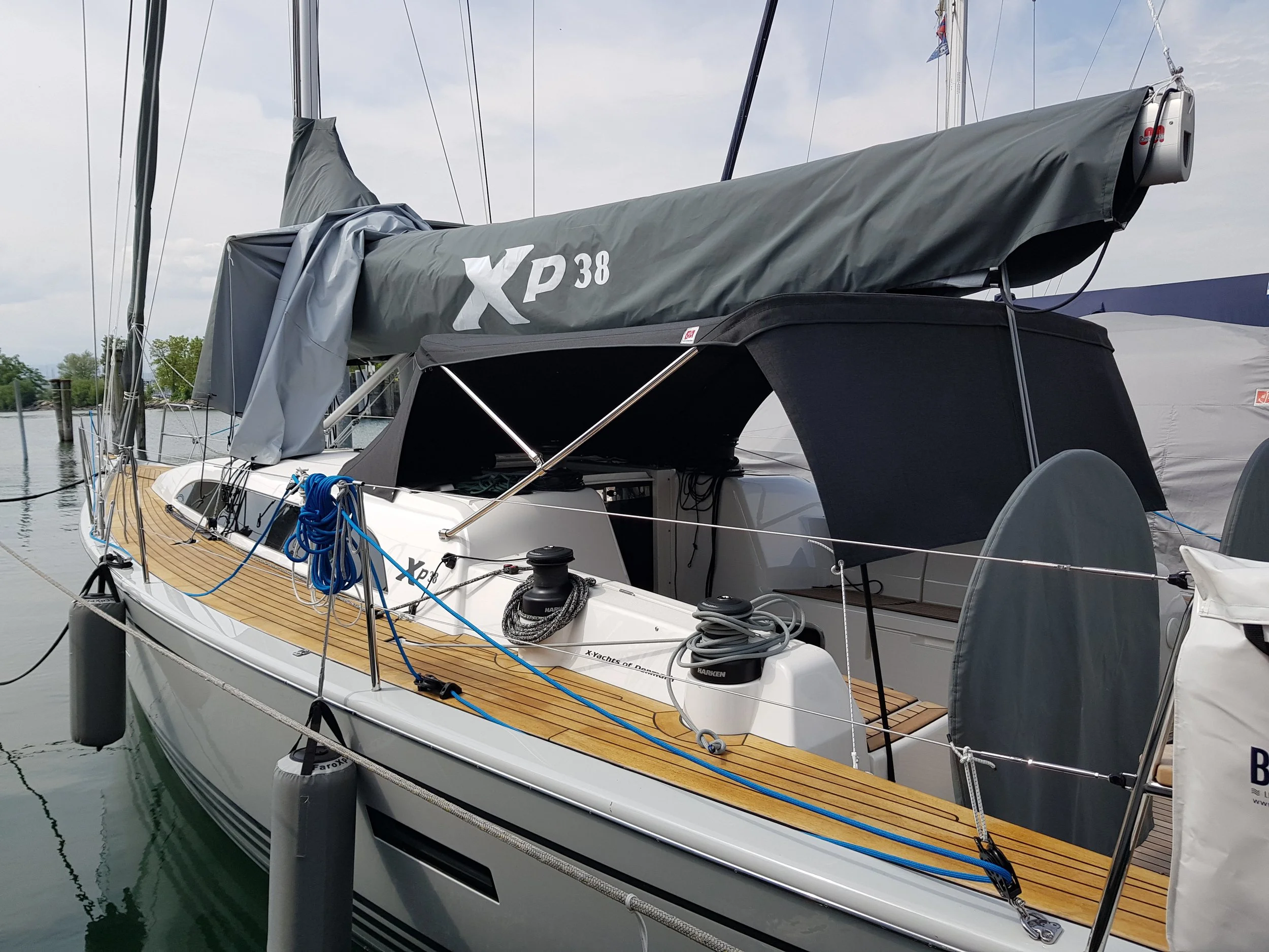 Segelboot mit der Aufschrift XP 38 im Hafen vertäut, mit grauem Segeltuch und blauen Seilen, sowie Teakholz-Deck.