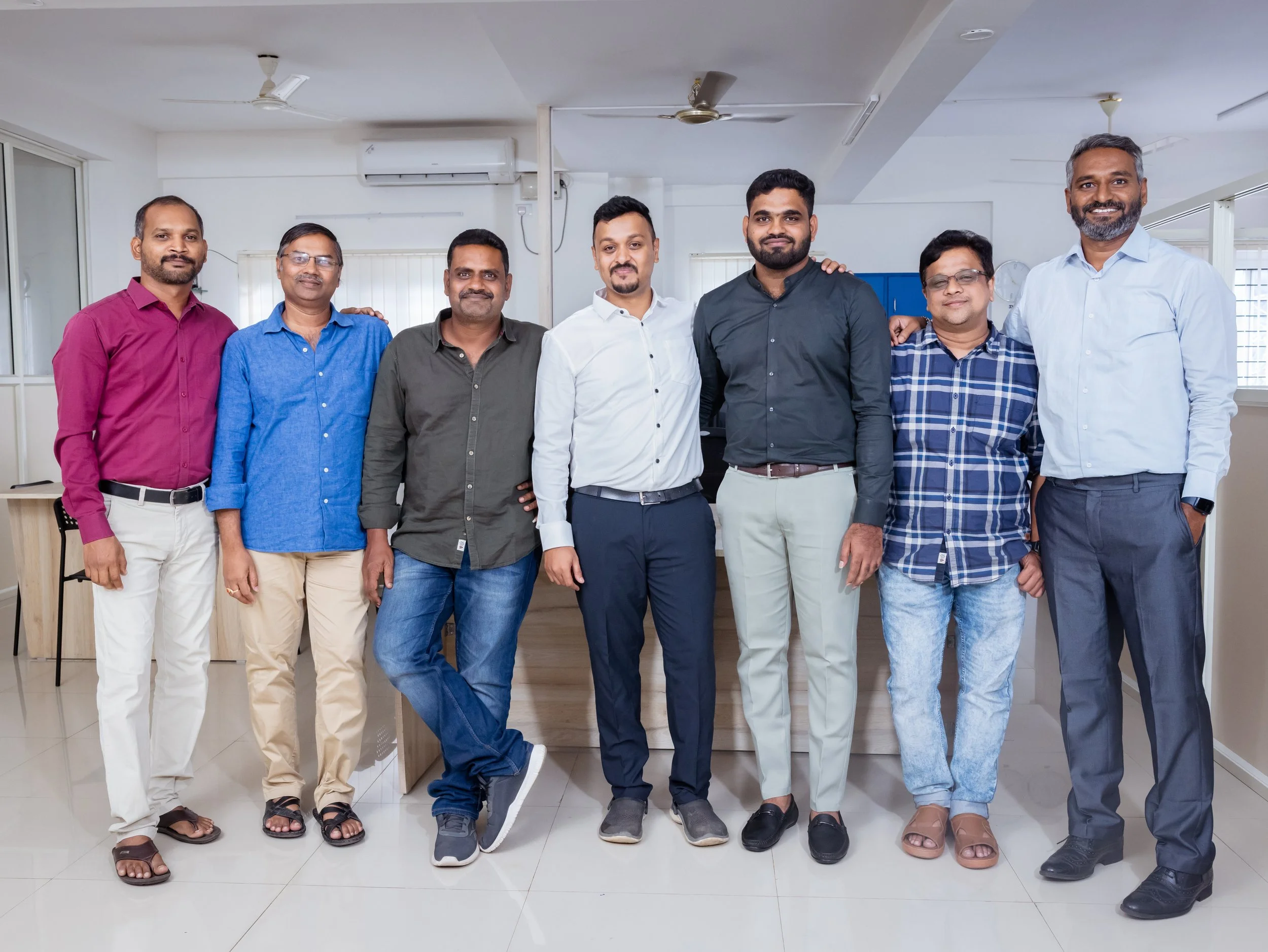 Groepe mensen staan samen in een kantoorruimte, glimlachend en gekleed in casual en zakelijke kleding.
