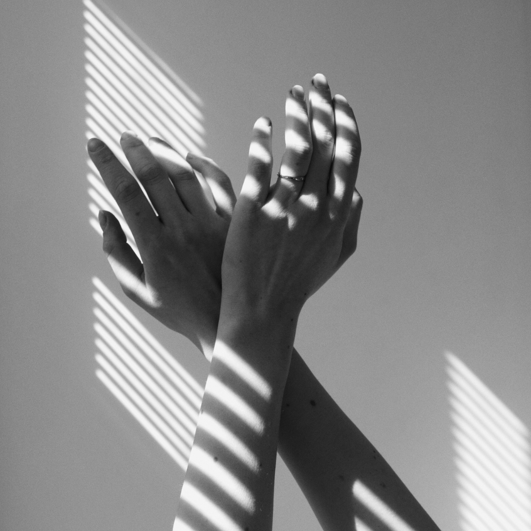 Mani femminili con mani incrociate, con ombreggiature di luci e ombre create da tende o persiane, in bianco e nero | Romina Felici - L'Officina dell'Io Art Coaching