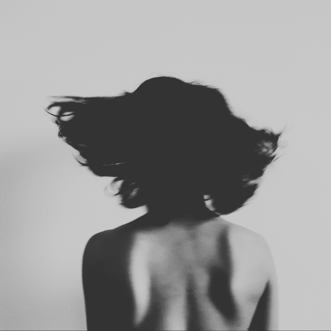 Siluetta di una donna senza capelli con schiena nuda, sfondo bianco e ombra sullo schermo.