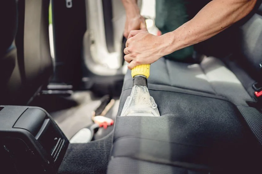 Person cleaning car seat with a handheld vacuum cleaner.