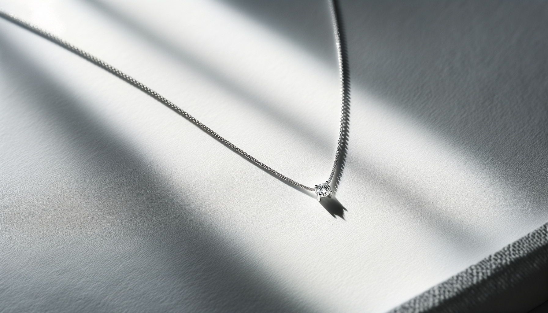 A silver chain necklace with a diamond pendant, displayed on a satin fabric background.