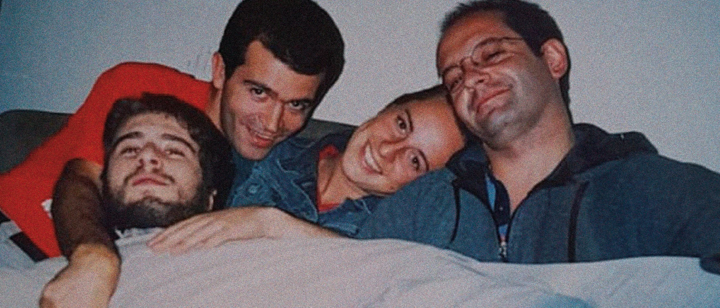 Cinque persone sorridenti che si rilassano e ridono insieme, sdraiate su un letto o divano.