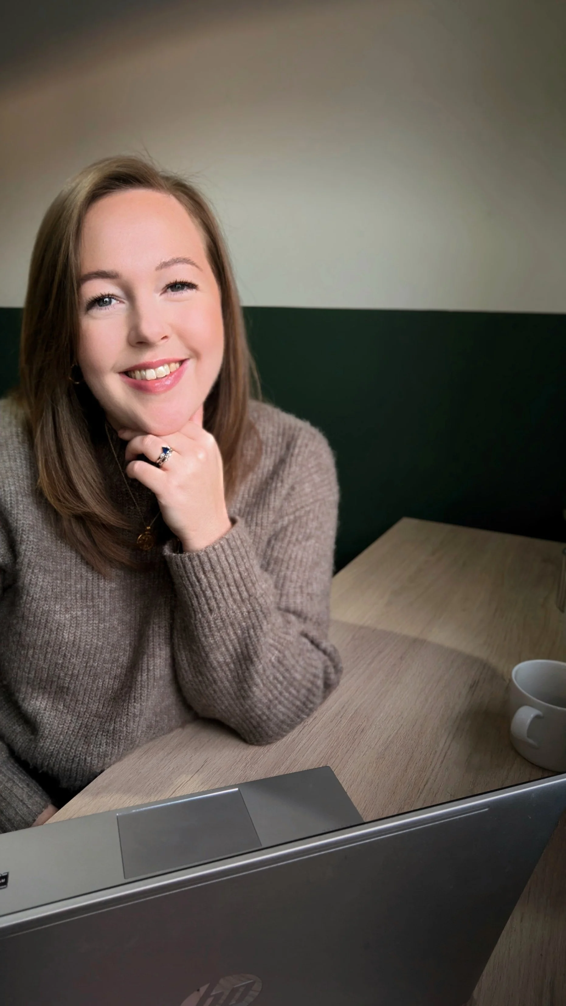 Woman smiling at a desk with a laptop and a cup of coffee.