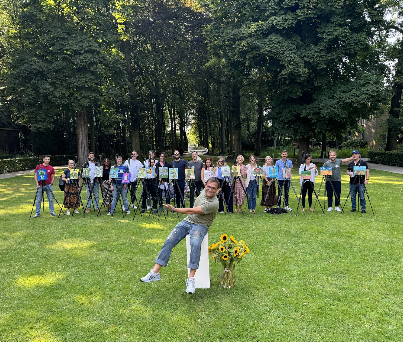 A group of stβArt participants proudly displaying their finished paintings on easels in a lush park, showcasing the collaborative spirit of art classes, workshops, and team building activities in Amsterdam.