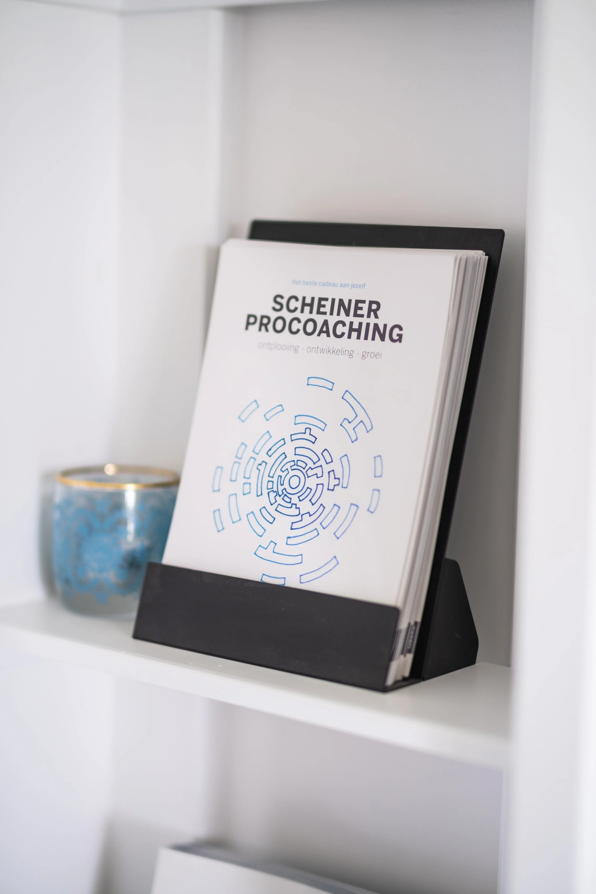 Vrouw zit aan tafel, heeft een pen in hand, en spreekt met een persoon die niet zichtbaar is.