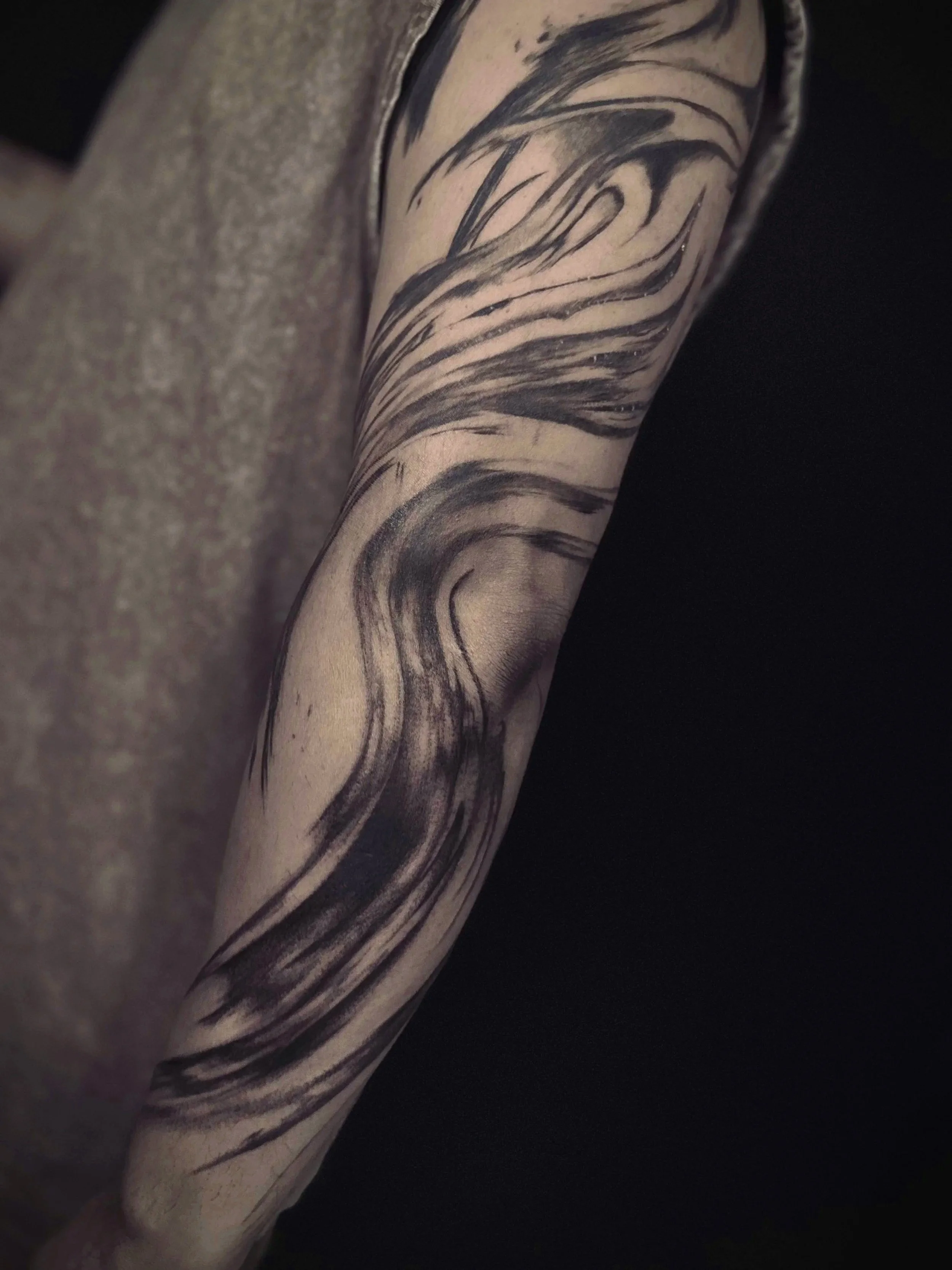 Close-up of a person's arm with a black ink tattoo featuring swirling abstract lines.