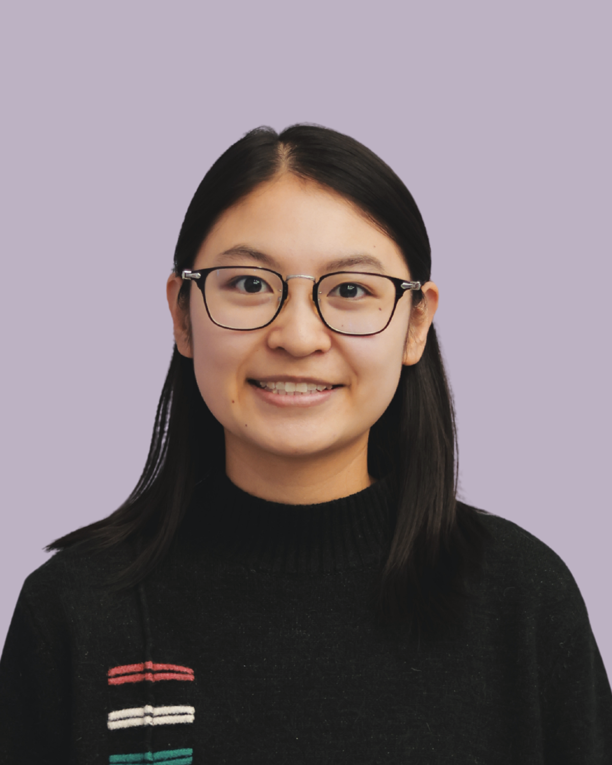 Portrait of a young woman with black hair, glasses, and a black sweater, smiling against a light purple background.