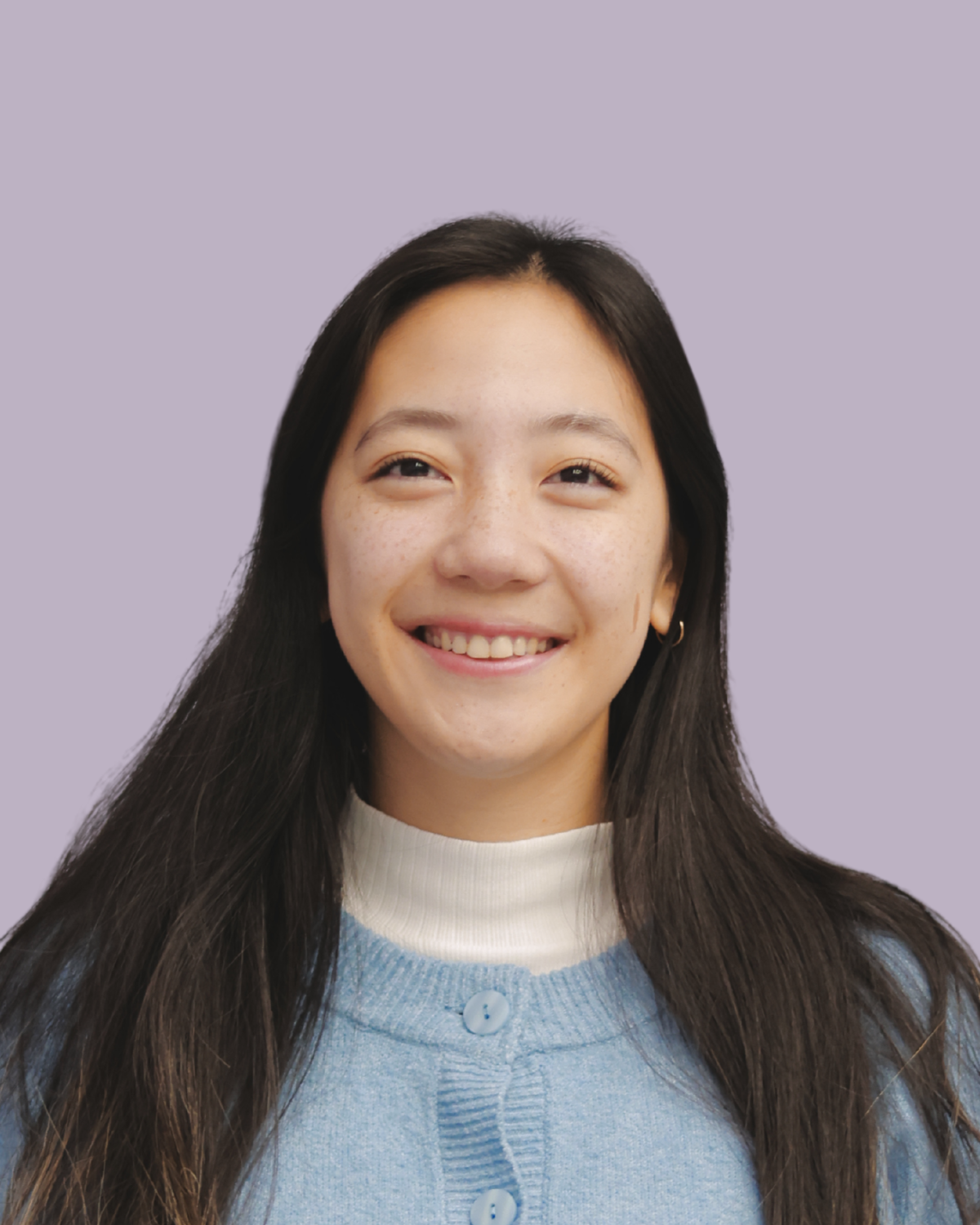 Portrait of a young woman with long dark hair, smiling, wearing a light blue sweater and white turtleneck, with a lavender background.