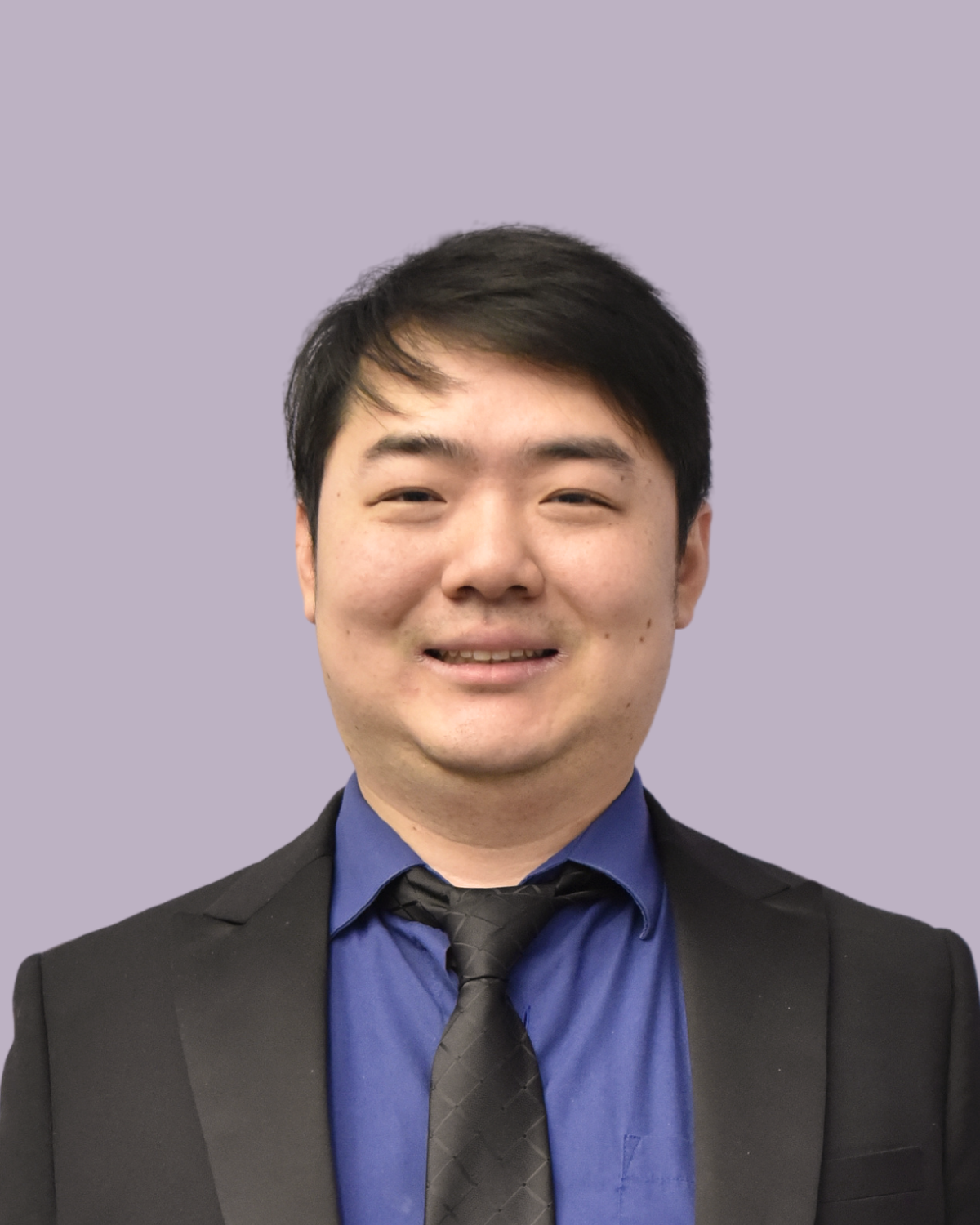 Headshot of a young man in a suit and tie, smiling, against a light purple background.