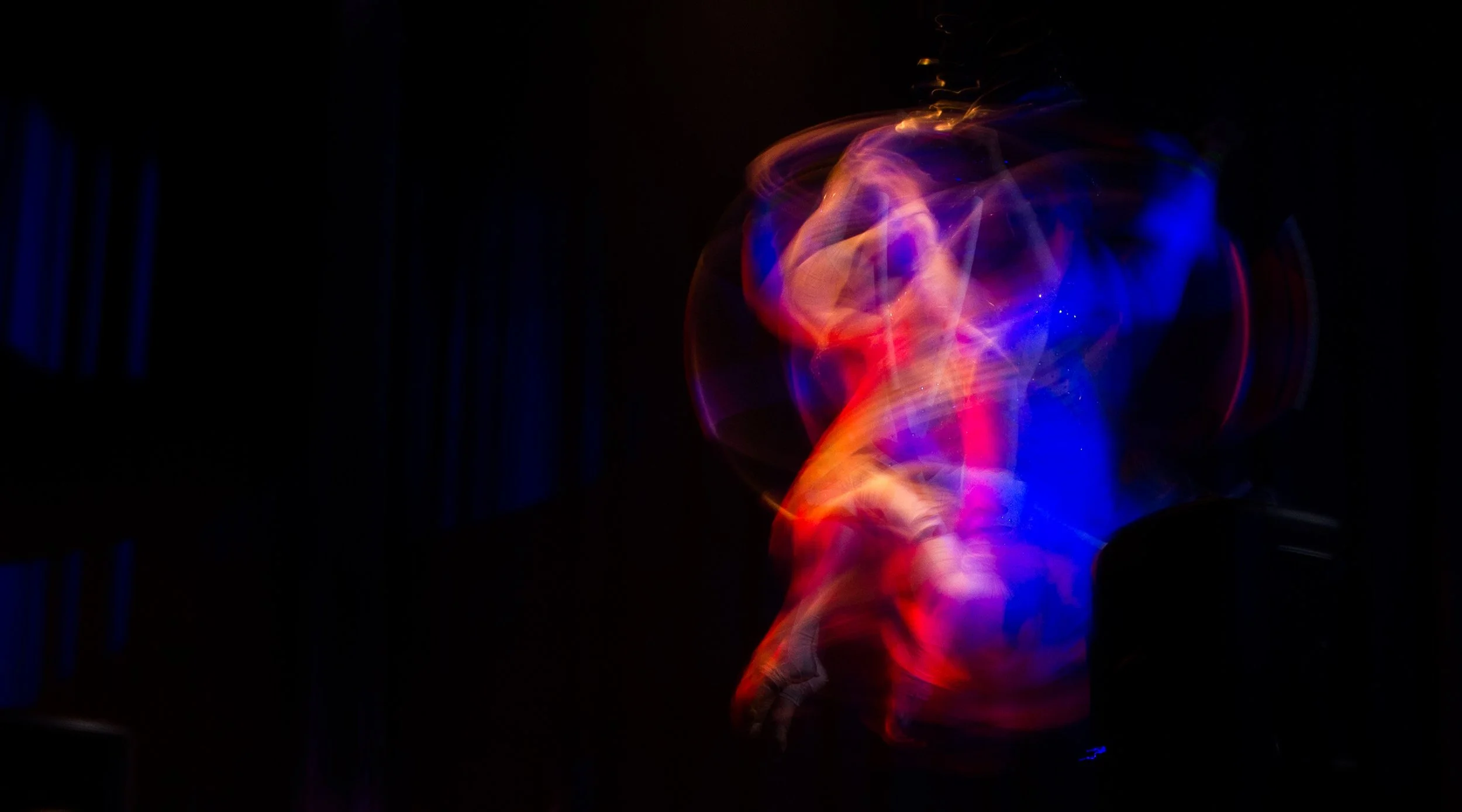 Blurred motion capture of a dancer with neon lights creating swirling patterns in dark surroundings.