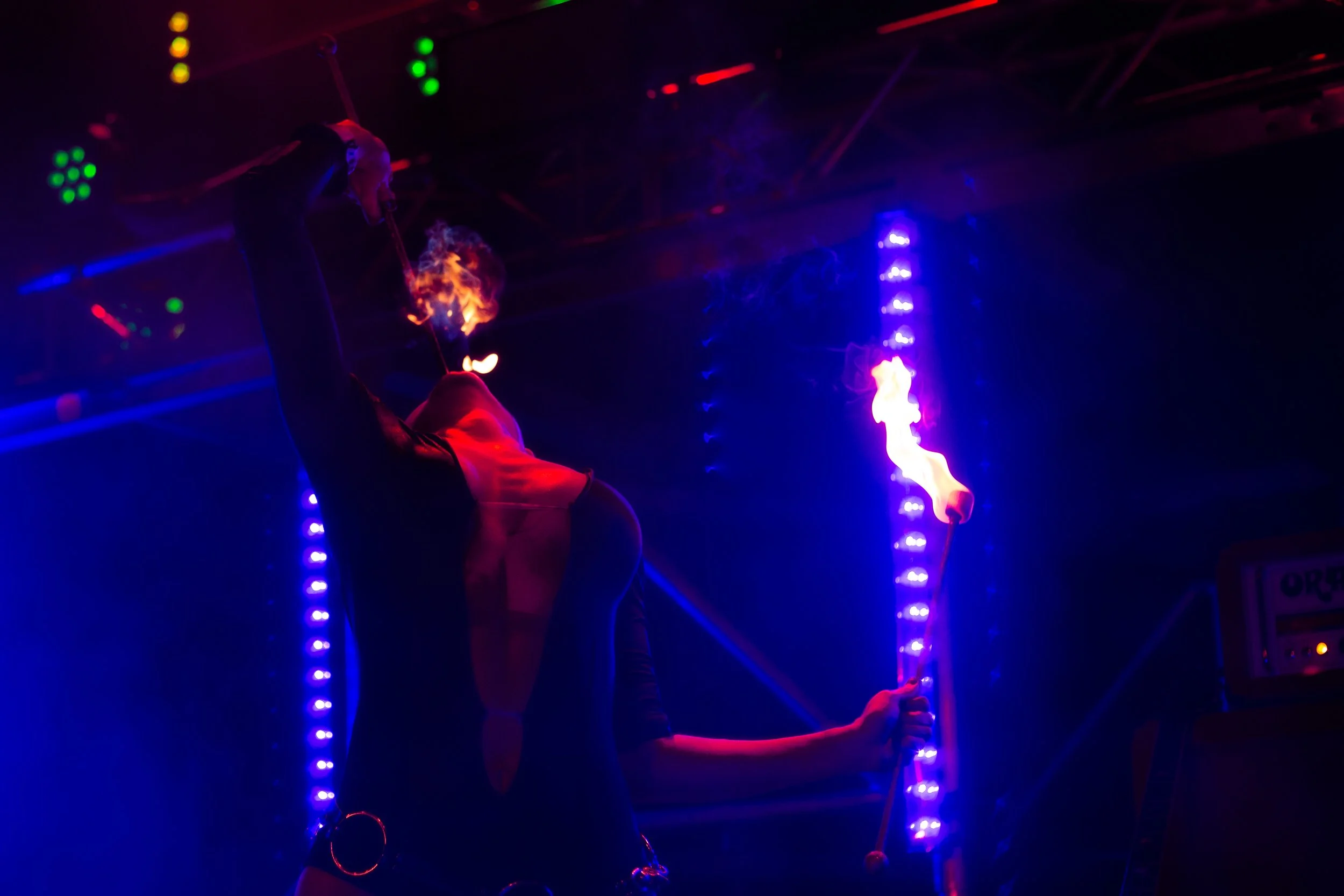 A performer on stage eating fire under colorful LED lights.