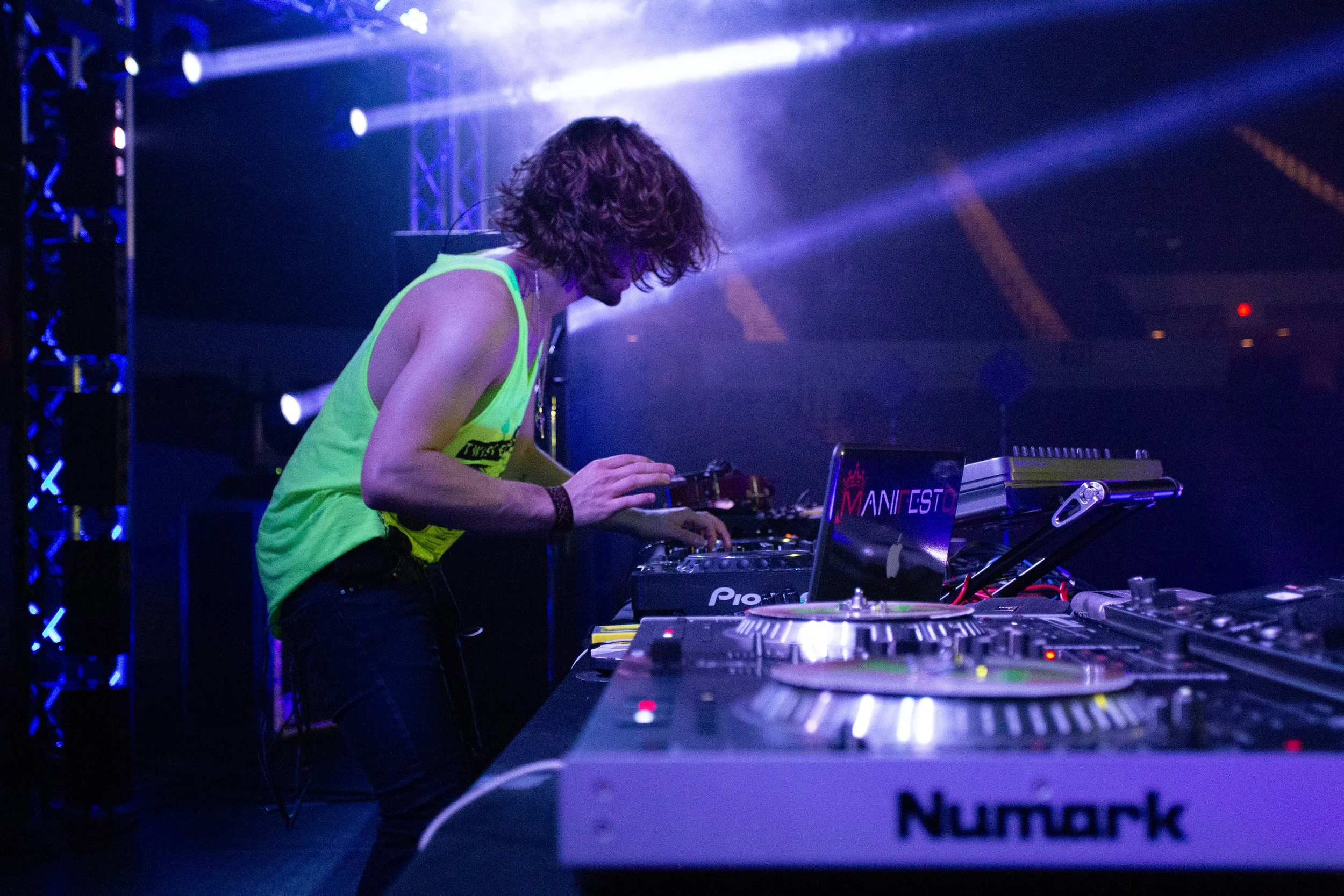 DJ performing live on stage with equipment and colorful lights.