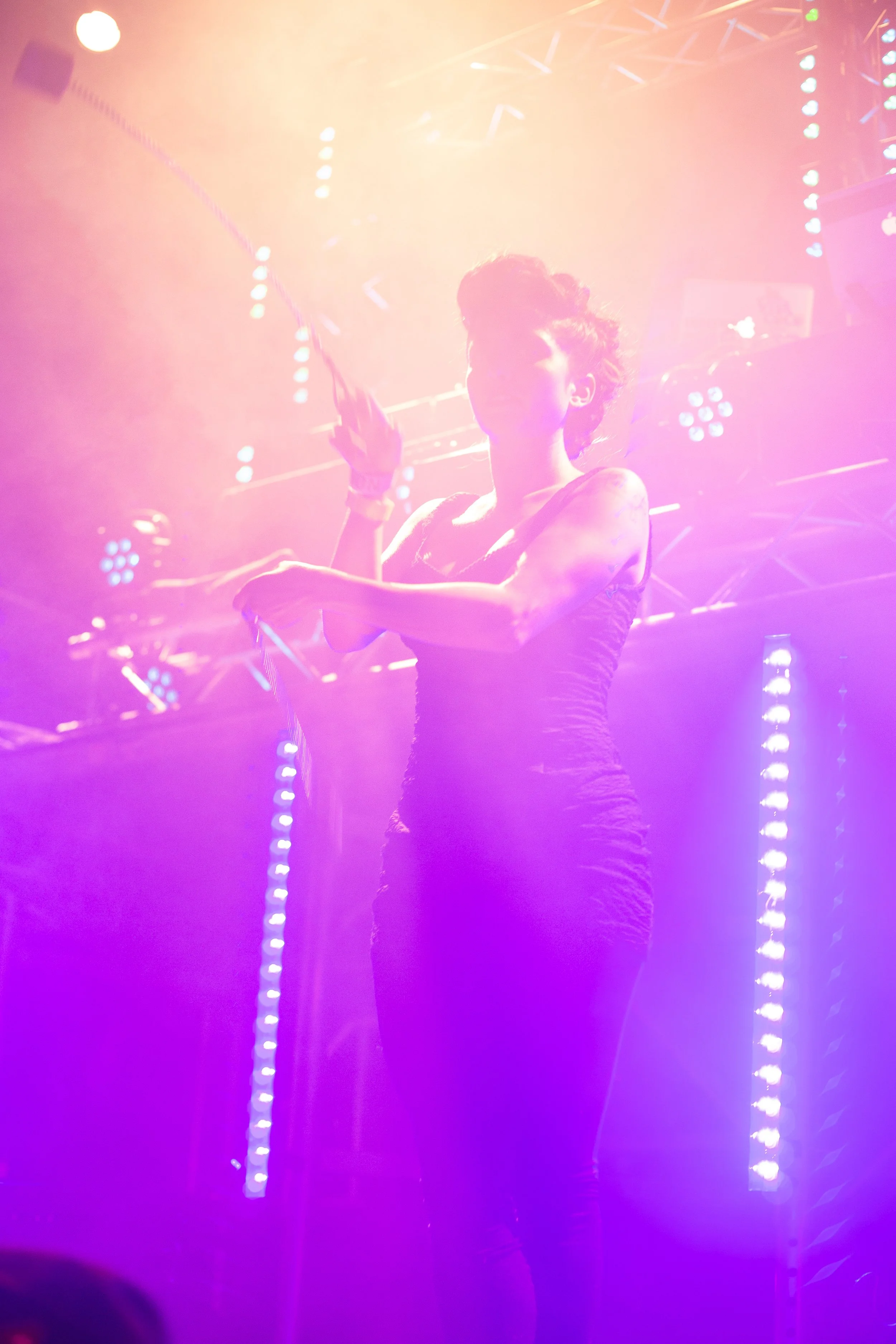 Person on stage under colorful stage lights, holding a whip with smoke effects.
