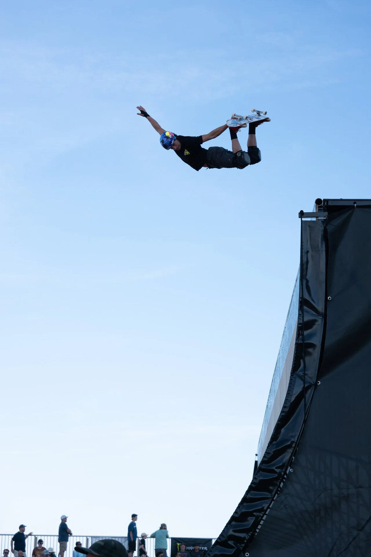 Skateboarder performing aerial trick on half-pipe ramp against blue sky.