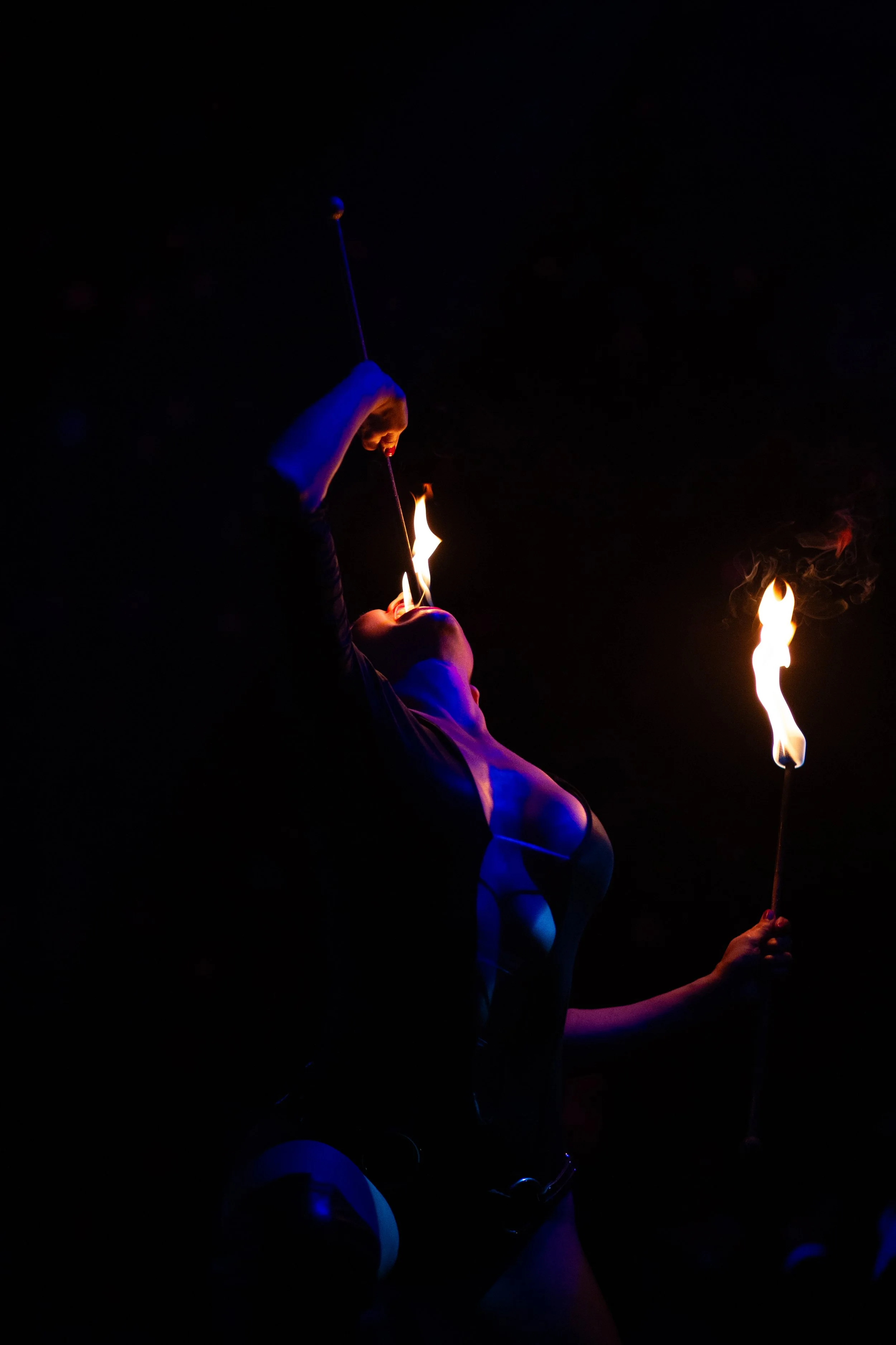 A person performing a fire-eating act in the dark, holding a flaming torch.