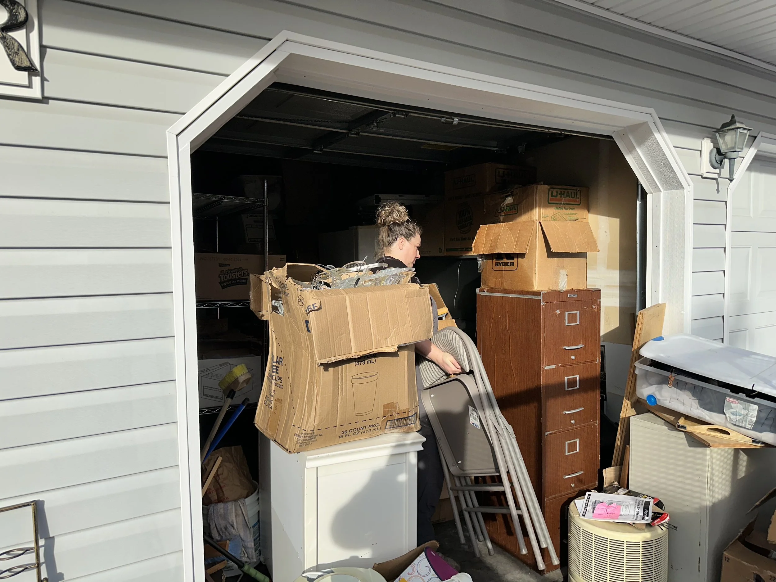 Team member sorting boxes and furniture inside a heavily cluttered garage during a cleanout project