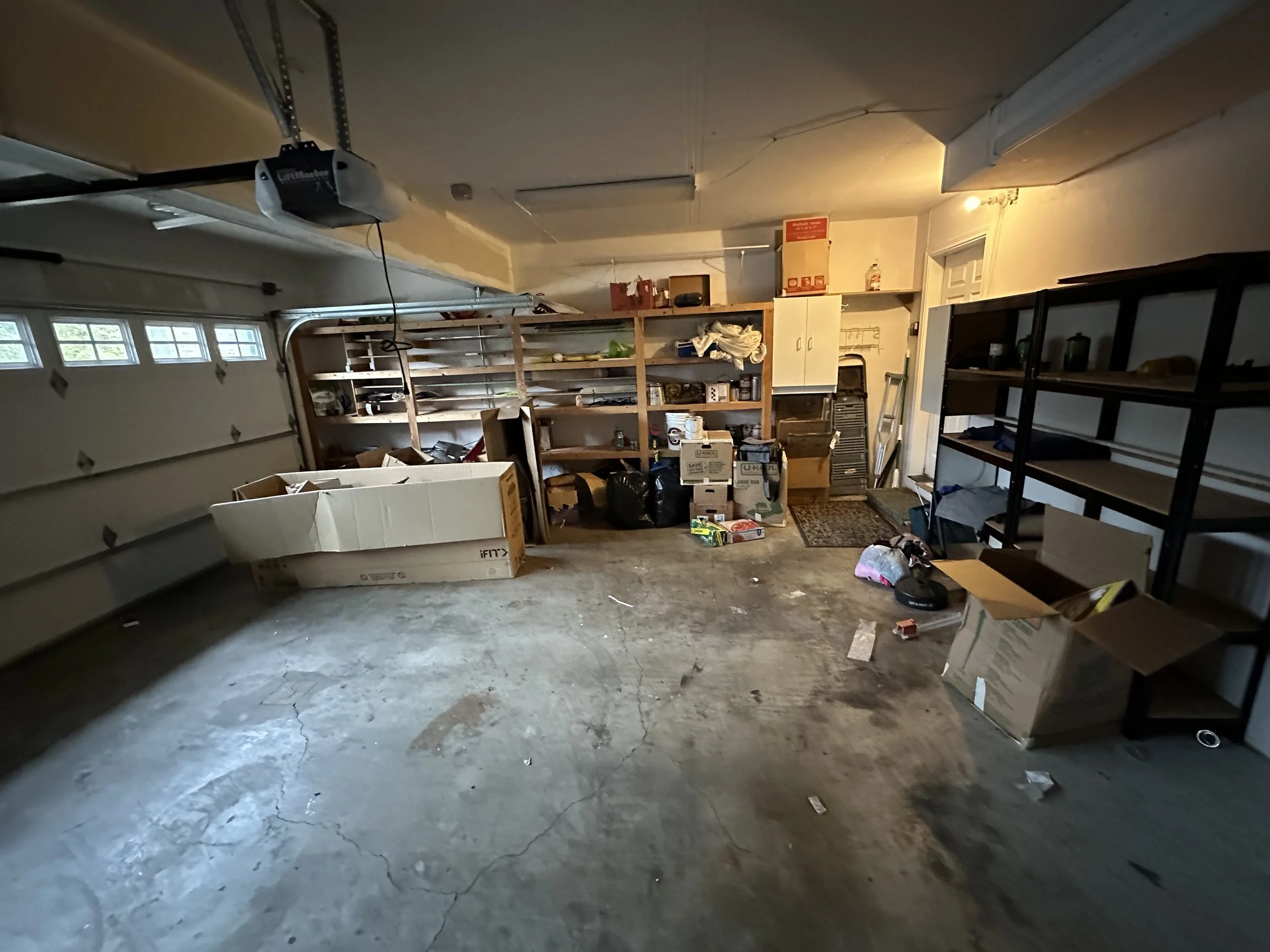Garage partially cleared with items moved to shelves and walls to prepare for sorting and junk removal