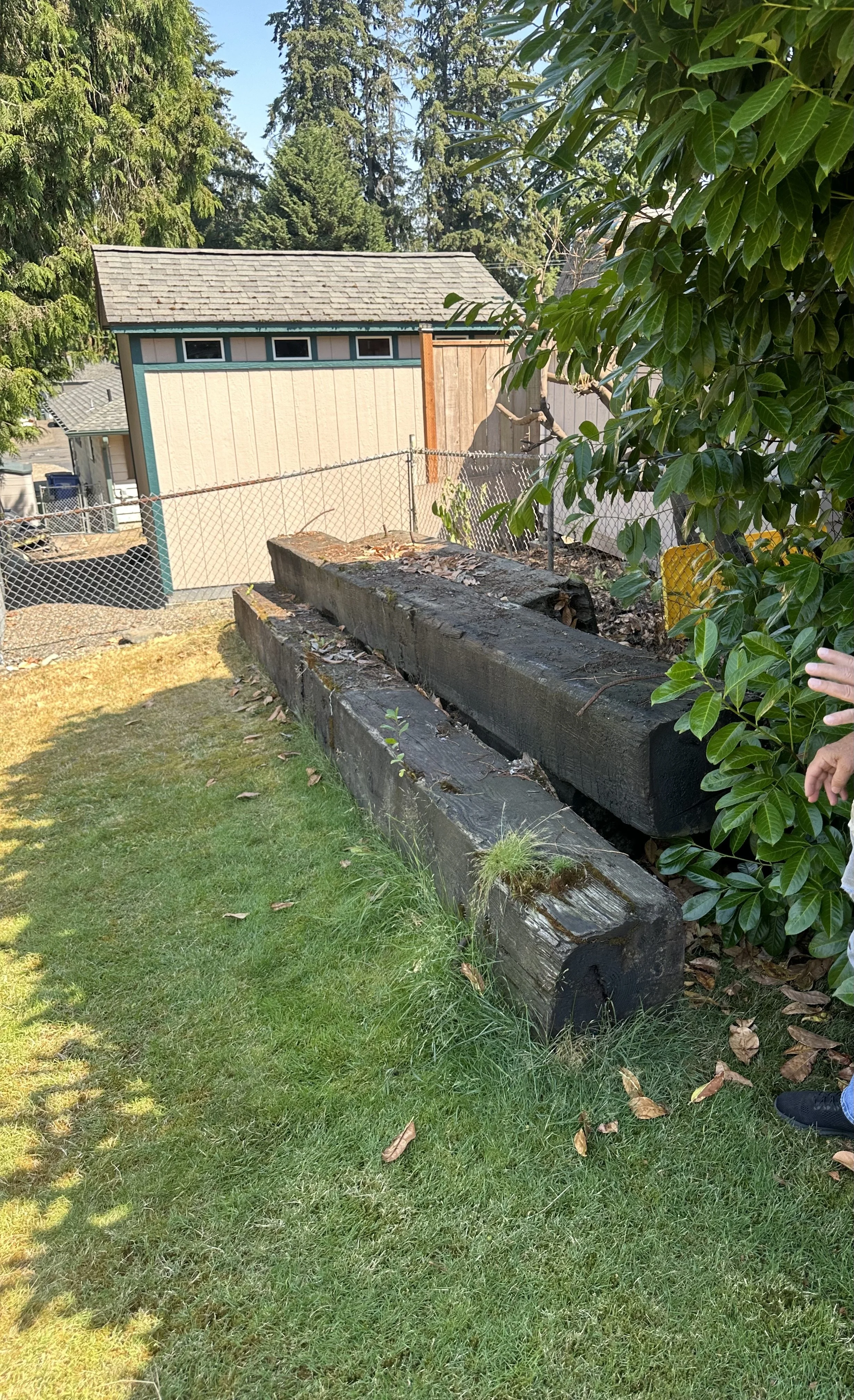 Before tear-down — large 20-ft retaining wall beams stacked in the customer’s backyard, Puyallup WA.