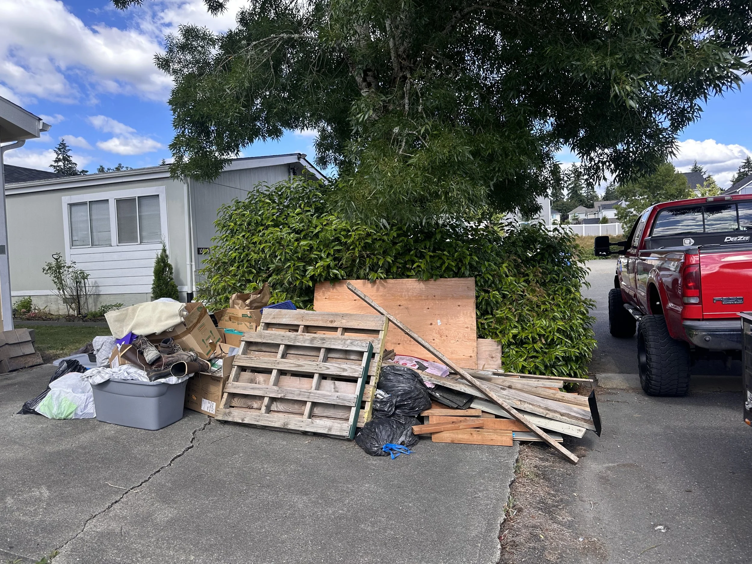 Pile of wooden pallets, scrap lumber, cardboard boxes, and household junk on a residential driveway in Puyallup, WA, before removal.