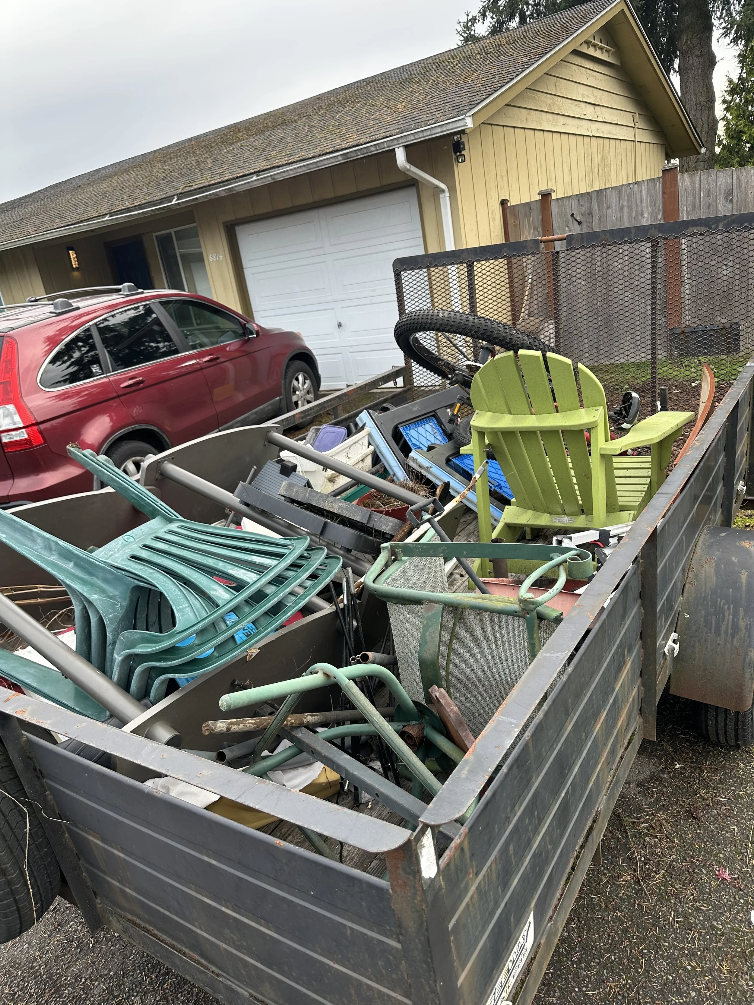 Trailer loaded with yard debris, planters, scrap wood, and outdoor junk removed from the property.