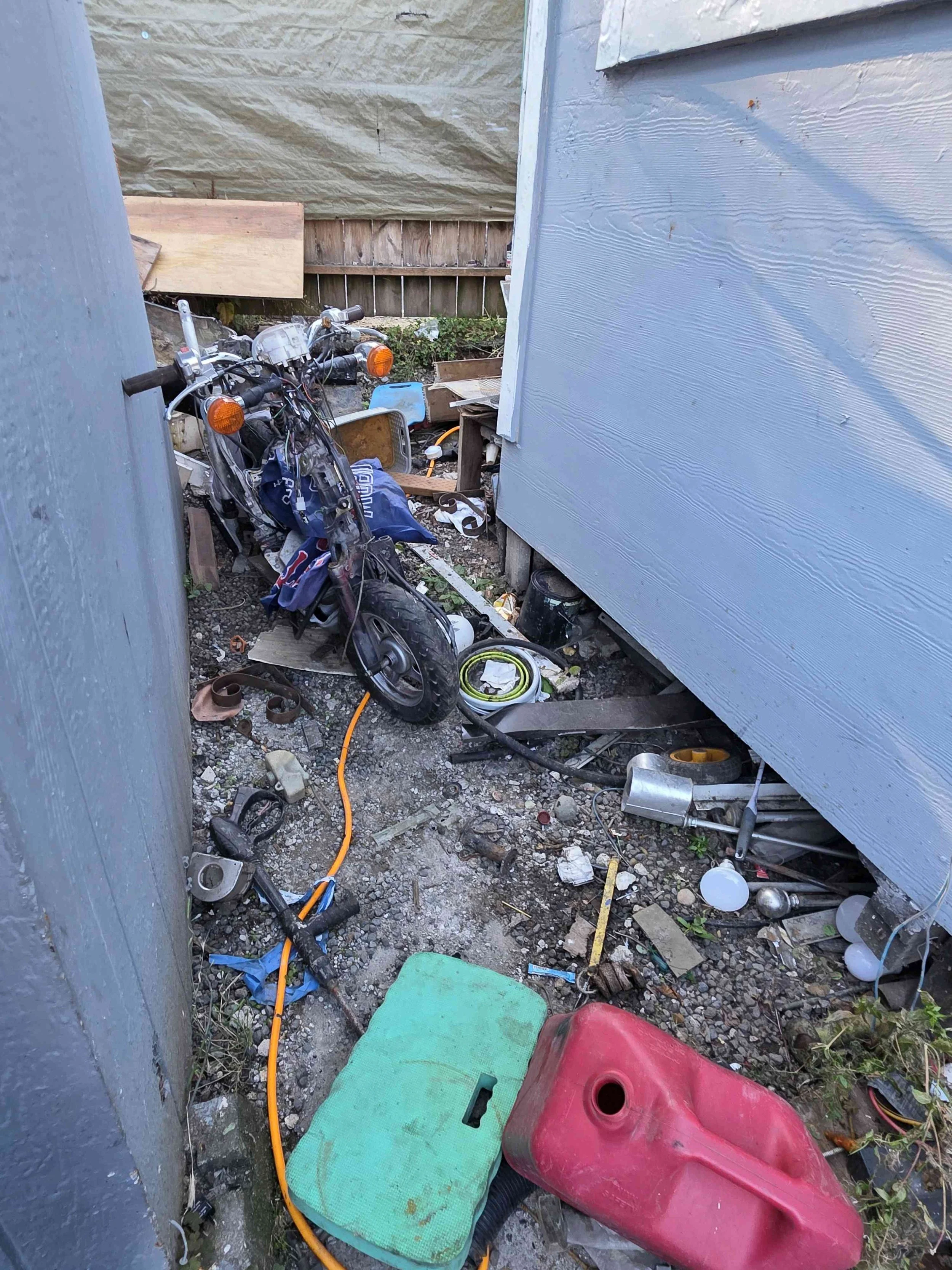 Motorcycle and scattered debris in a narrow passage between buildings at a Tukwila eviction cleanup property.