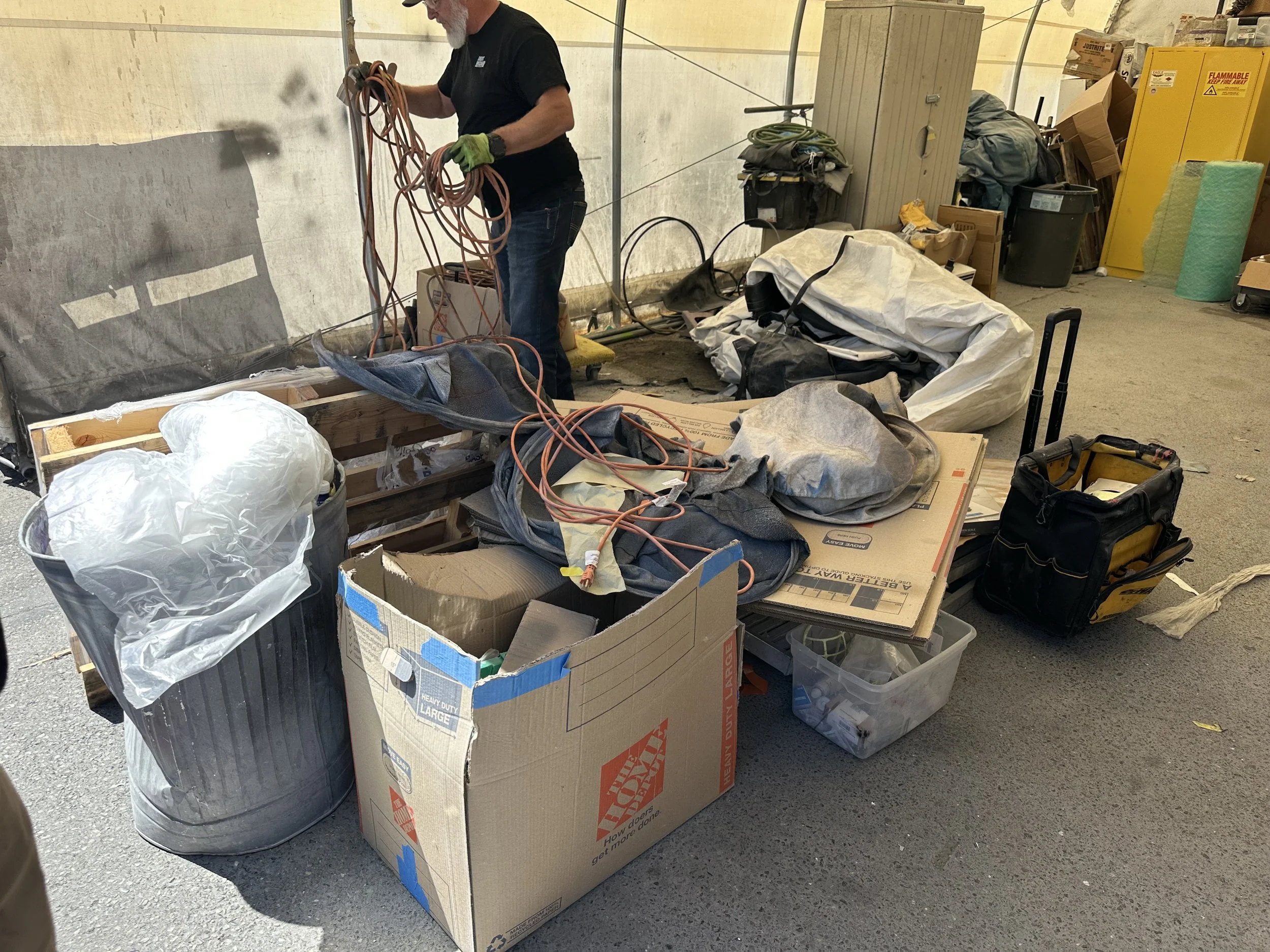 Automotive shop storage area with boxes, tarps, extension cords, and unwanted supplies before cleanout at Dent Wizard in Tukwila, WA.