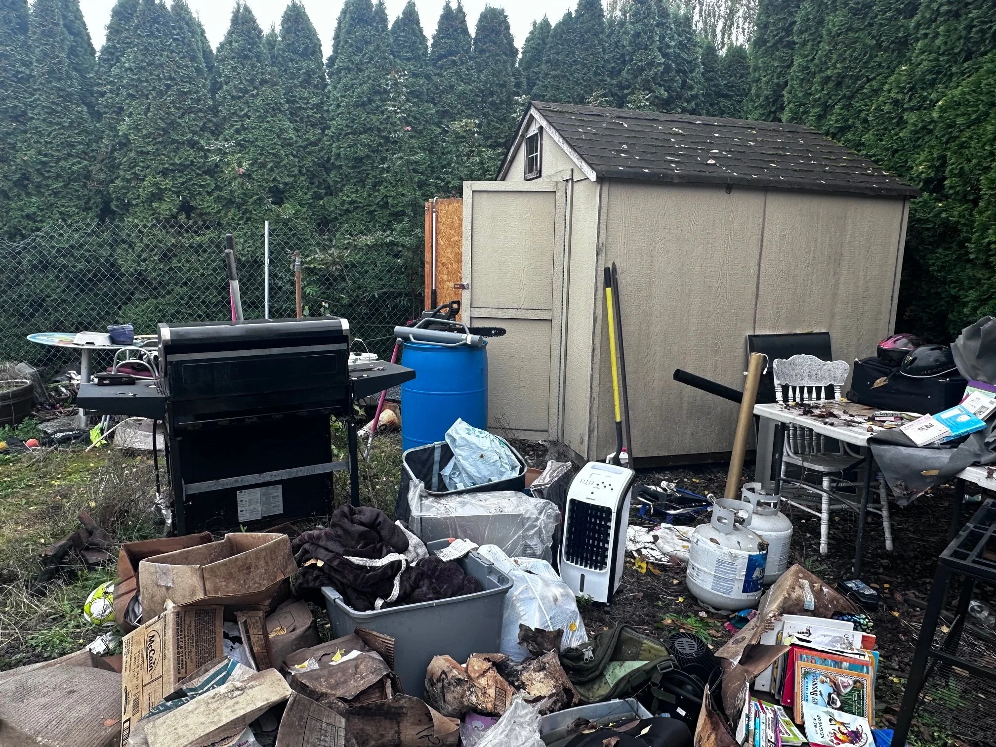 BEFORE — Old grill, propane tanks, and scattered items crowding the yard (Sumner, WA).