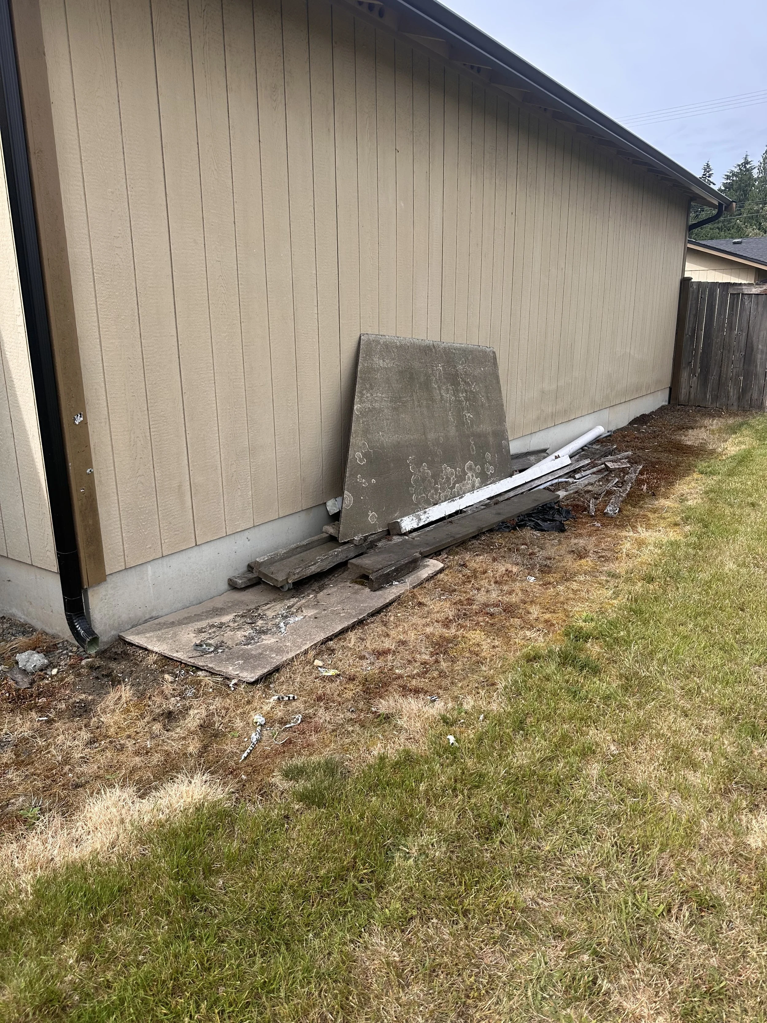Scrap wood, boards, and leftover building materials stacked along the outside wall of a home in Puyallup, WA.